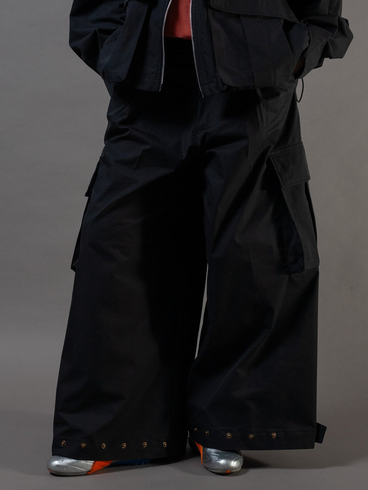 Person wearing a black outfit with wide-leg pants and a jacket on a gray background