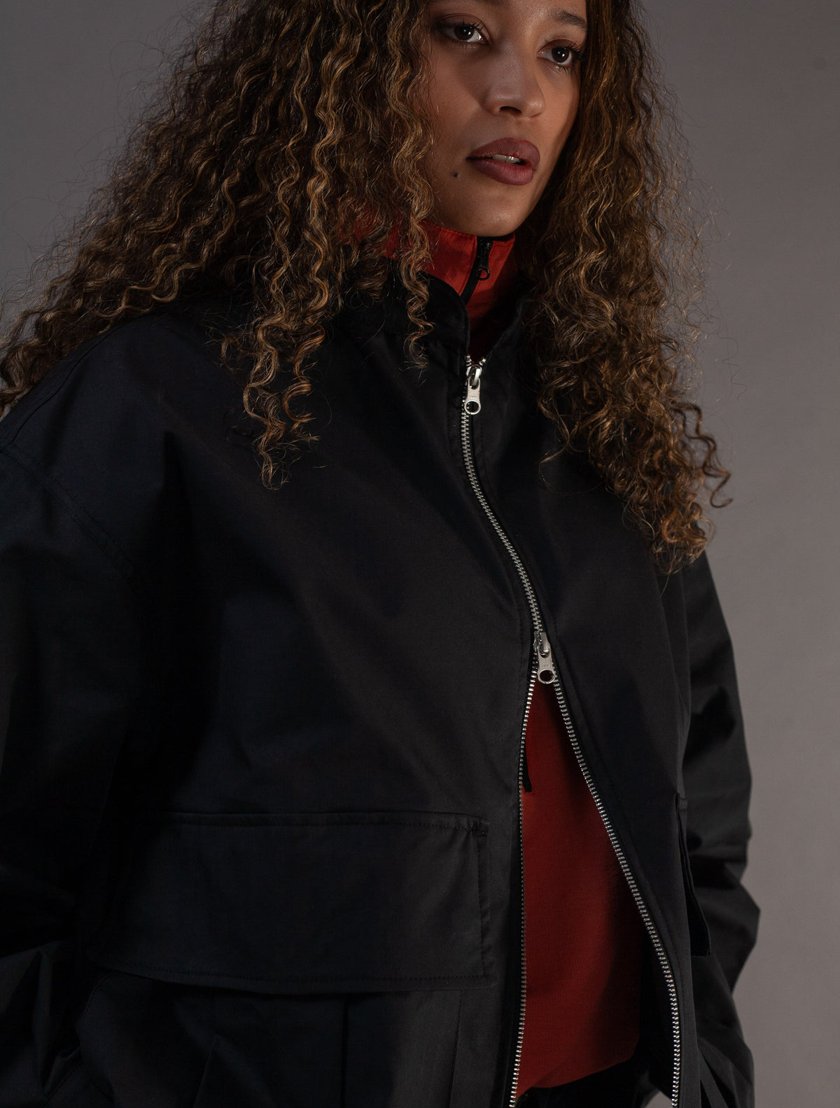 Person wearing a black jacket with a orange top underneath on a gray background