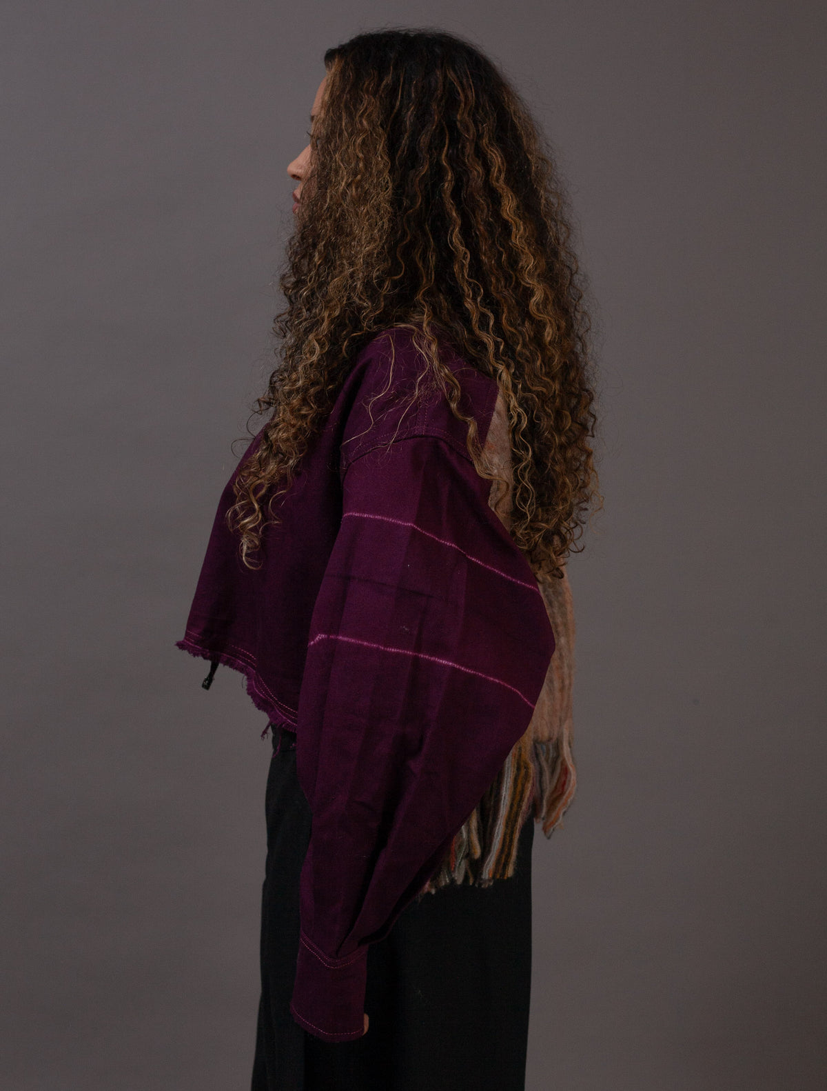 Person wearing a purple shawl with wool fringe on a gray background