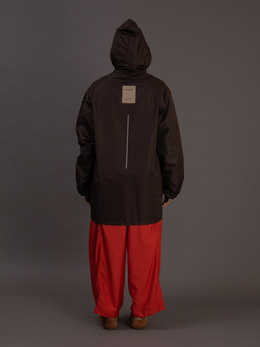 Person wearing a dark brown jacket and orange pants on a gray background