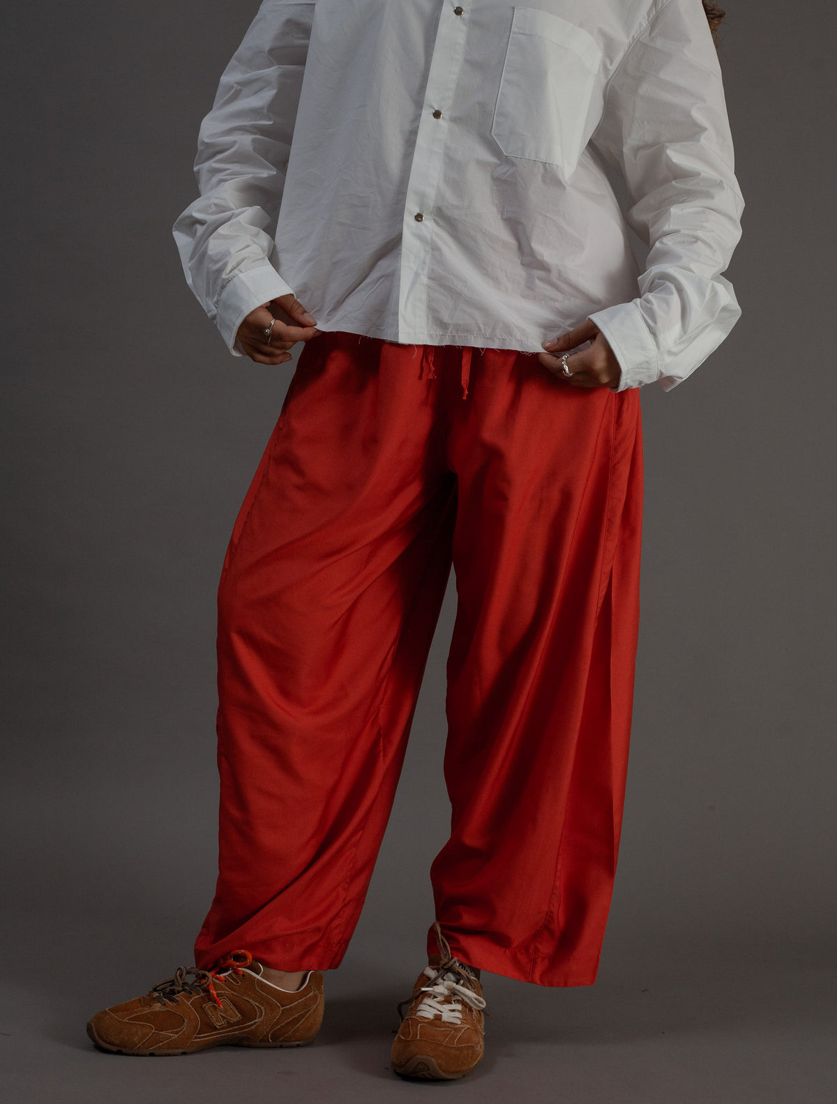 Person wearing a white shirt and orange pants on a gray background