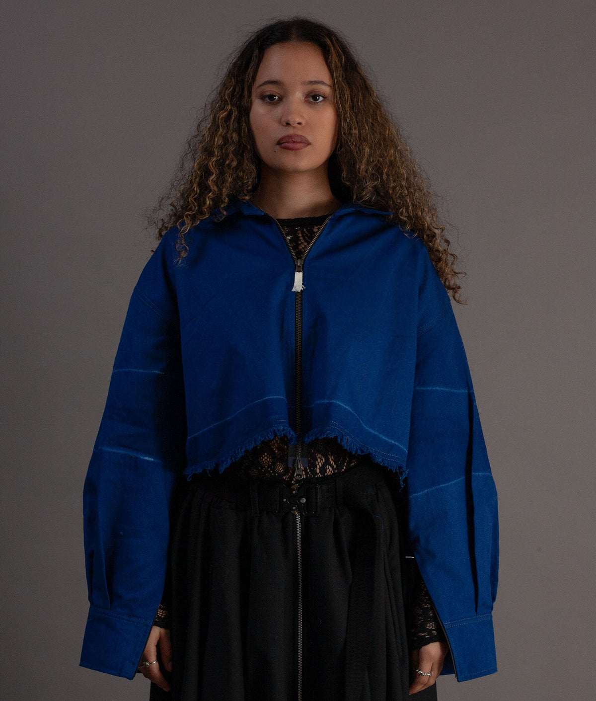 Woman wearing a blue jacket over a black outfit on a gray background