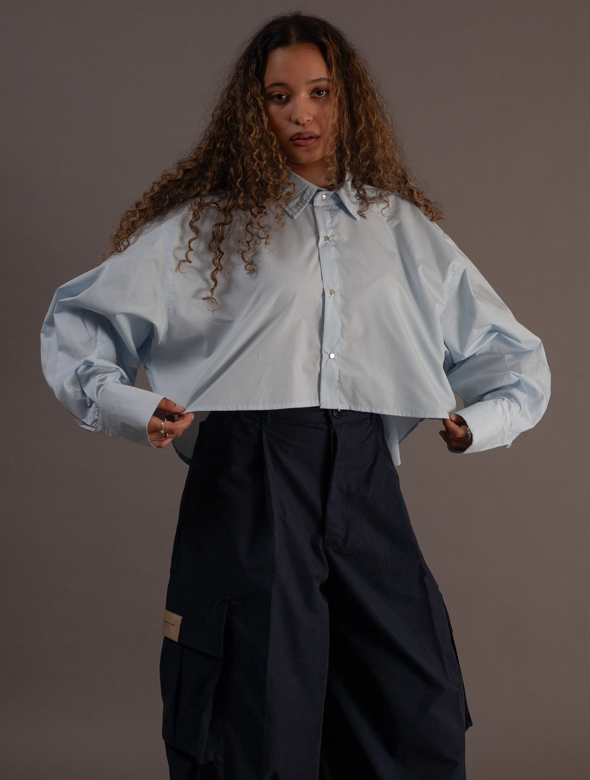 Woman wearing a light blue shirt and black pants against a gray background