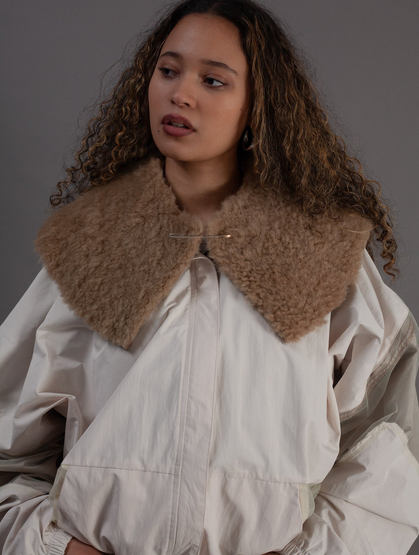 Woman wearing a beige coat with a fur collar against a gray background
