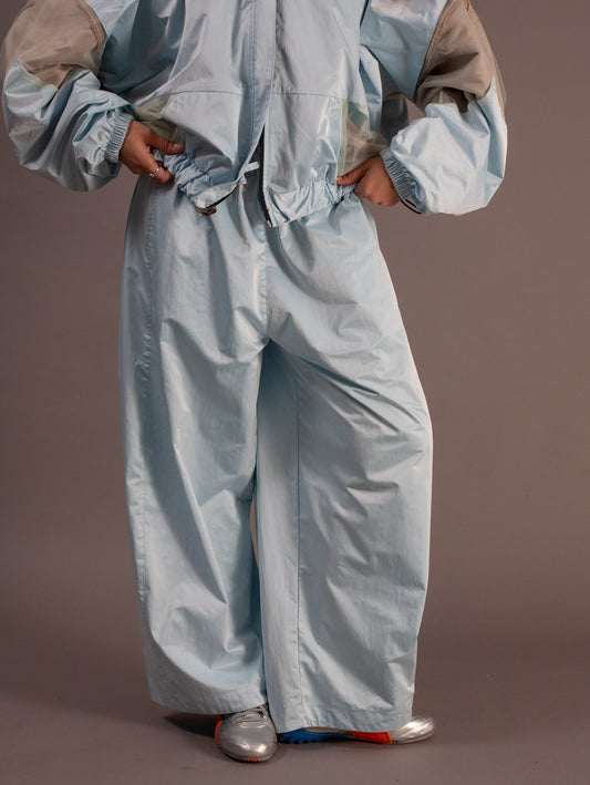 Person wearing a light blue sports jacket and pants on a brown background