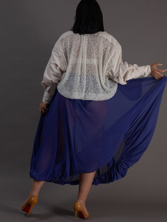 Person wearing a white lace top and purple mesh skirt on a gray background