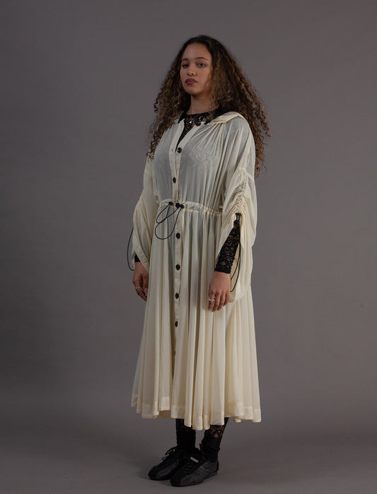 Person wearing a long, light-colored coat with black buttons