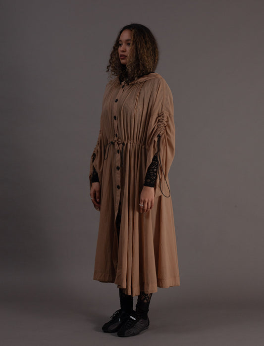 Woman wearing a long beige coat against a grey background