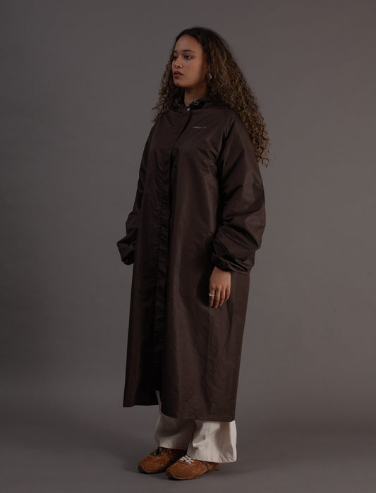 Person wearing a long brown raincoat against a grey background