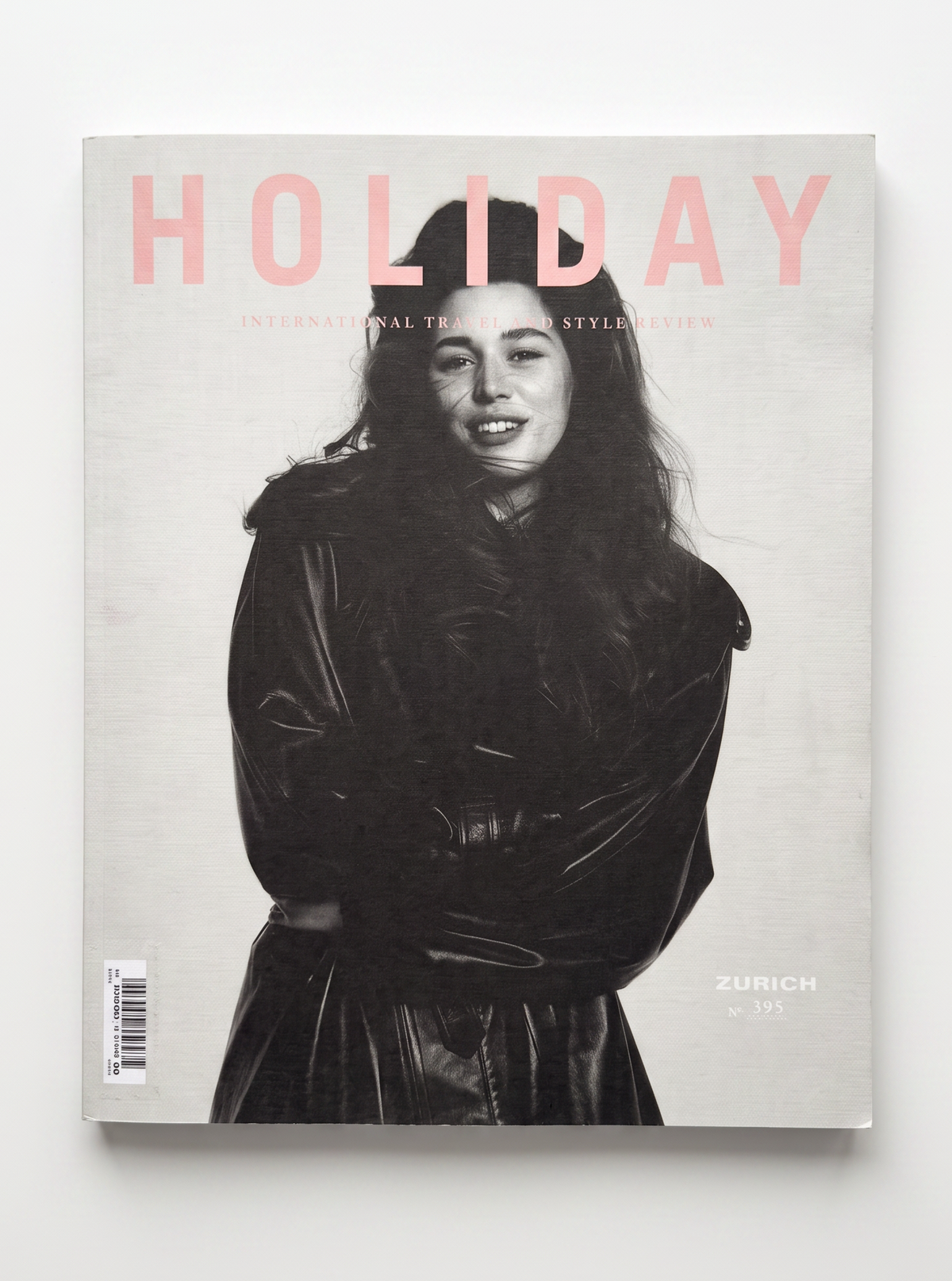 A magazine titled 'HOLIDAY' with a black-and-white portrait cover of a woman in a dark coat, photographed against a light gray background.