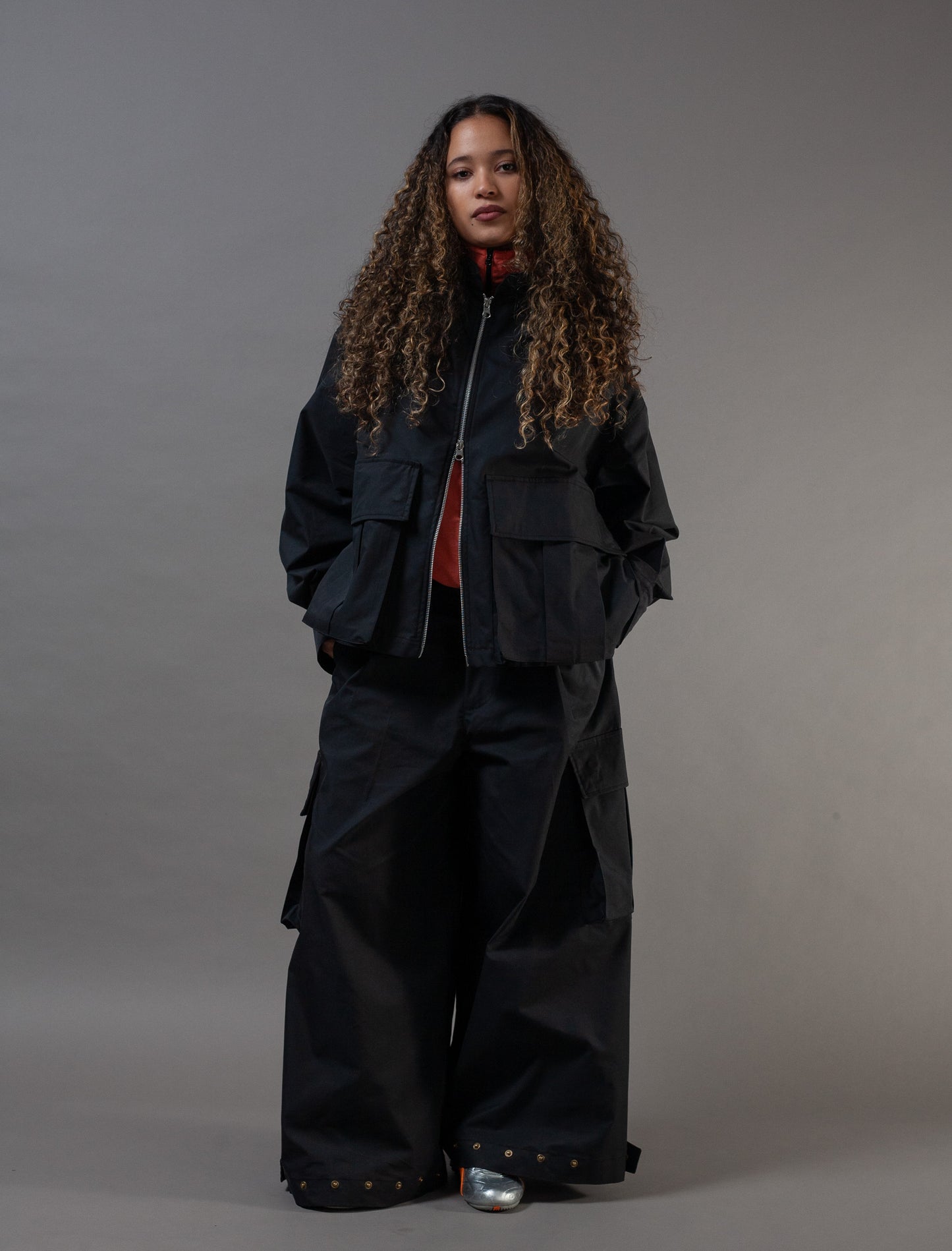 Person wearing a black outfit with a jacket and pants on a gray background