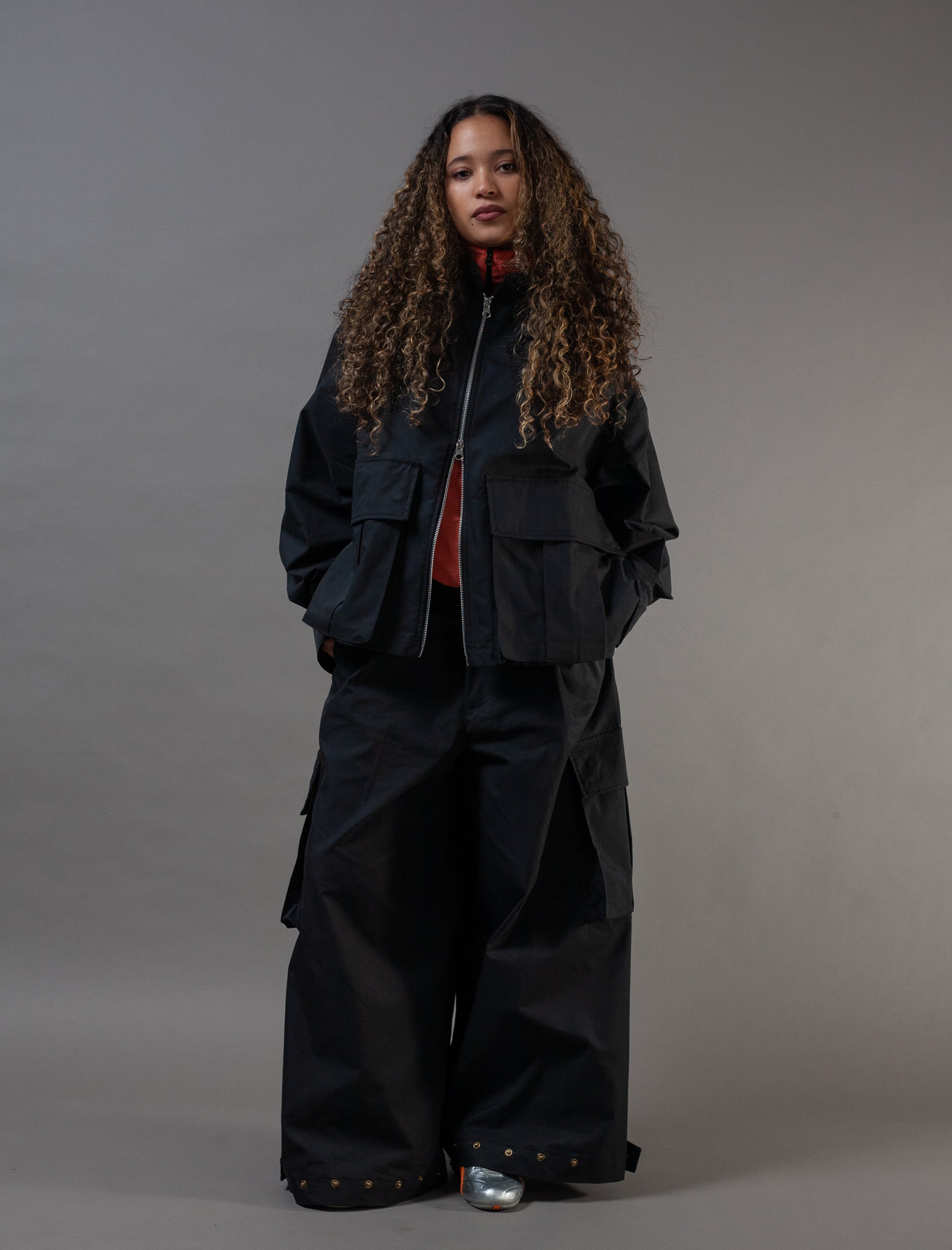 Person wearing a black outfit with a jacket and pants on a gray background