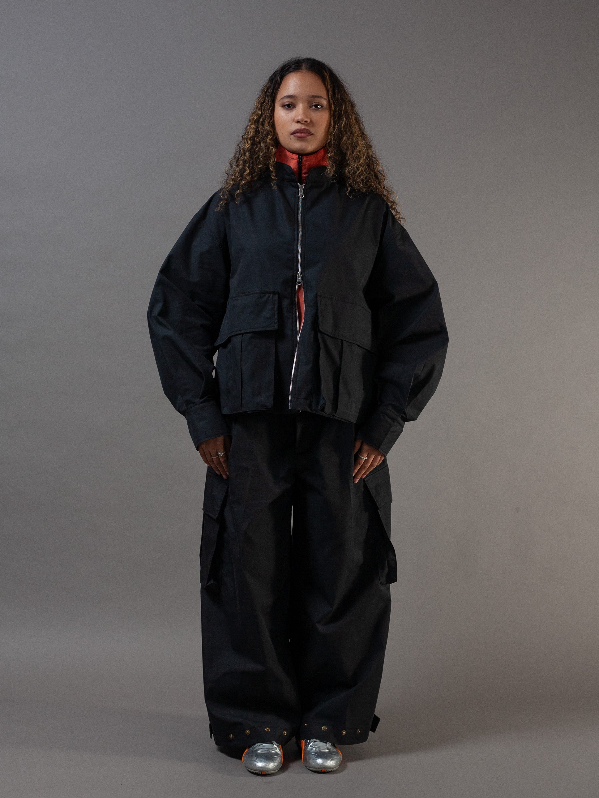 Person wearing a black outfit with a jacket and pants on a gray background