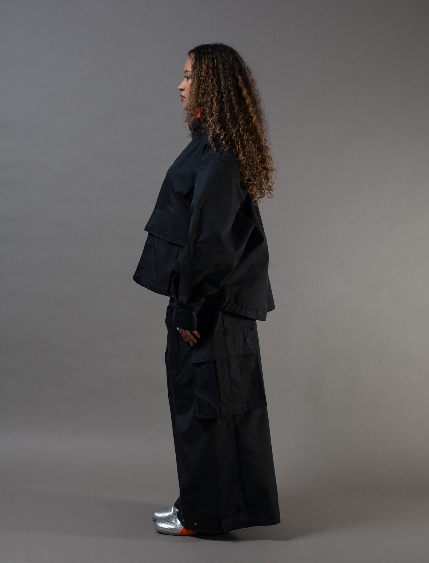 Person wearing a black outfit standing against a gray background