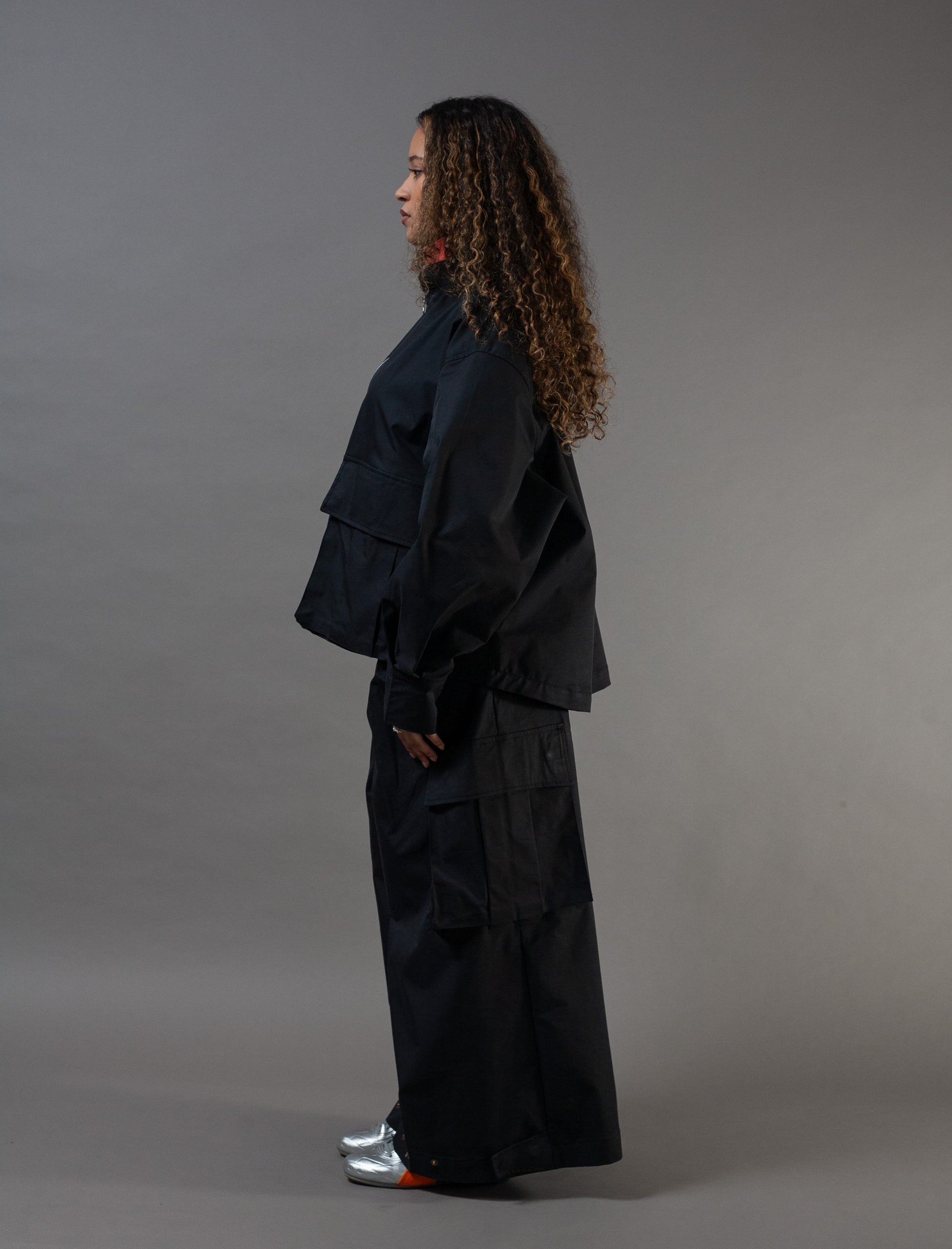 Person wearing a black outfit standing against a gray background