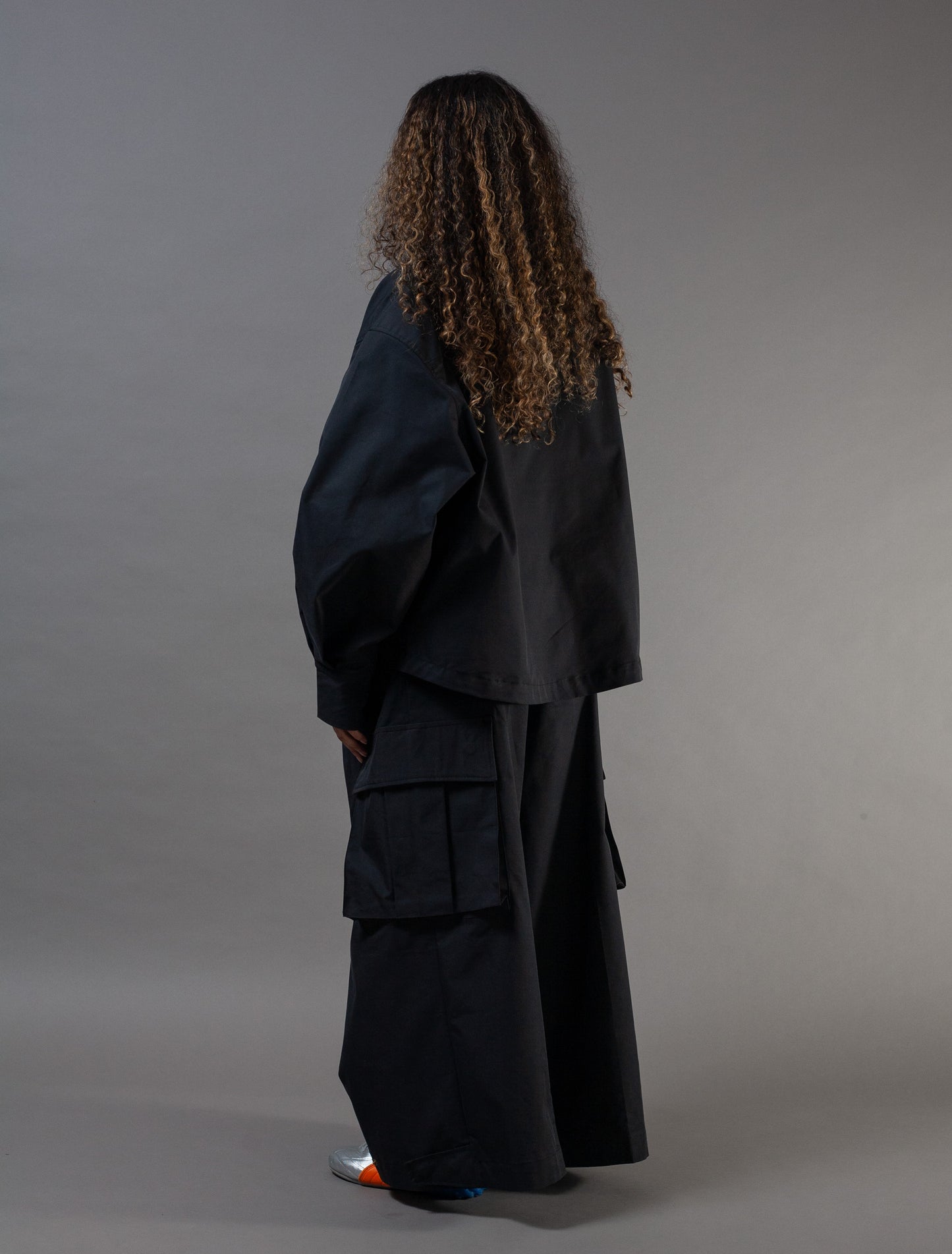 Person wearing a black outfit with wide pants on a gray background