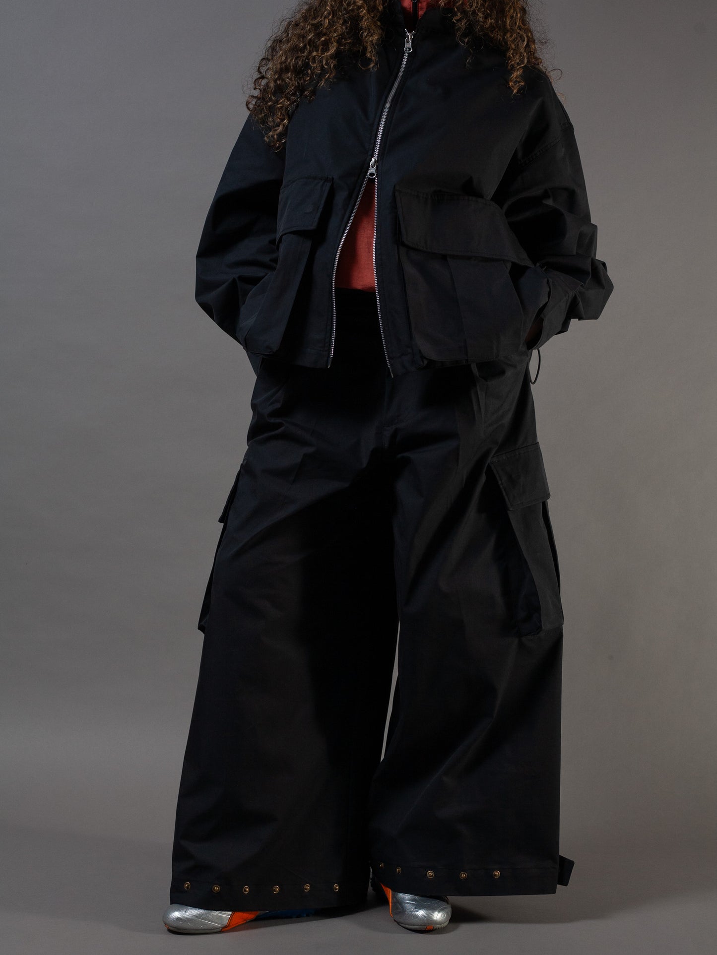 Person wearing a black outfit with wide-leg pants and a jacket on a gray background