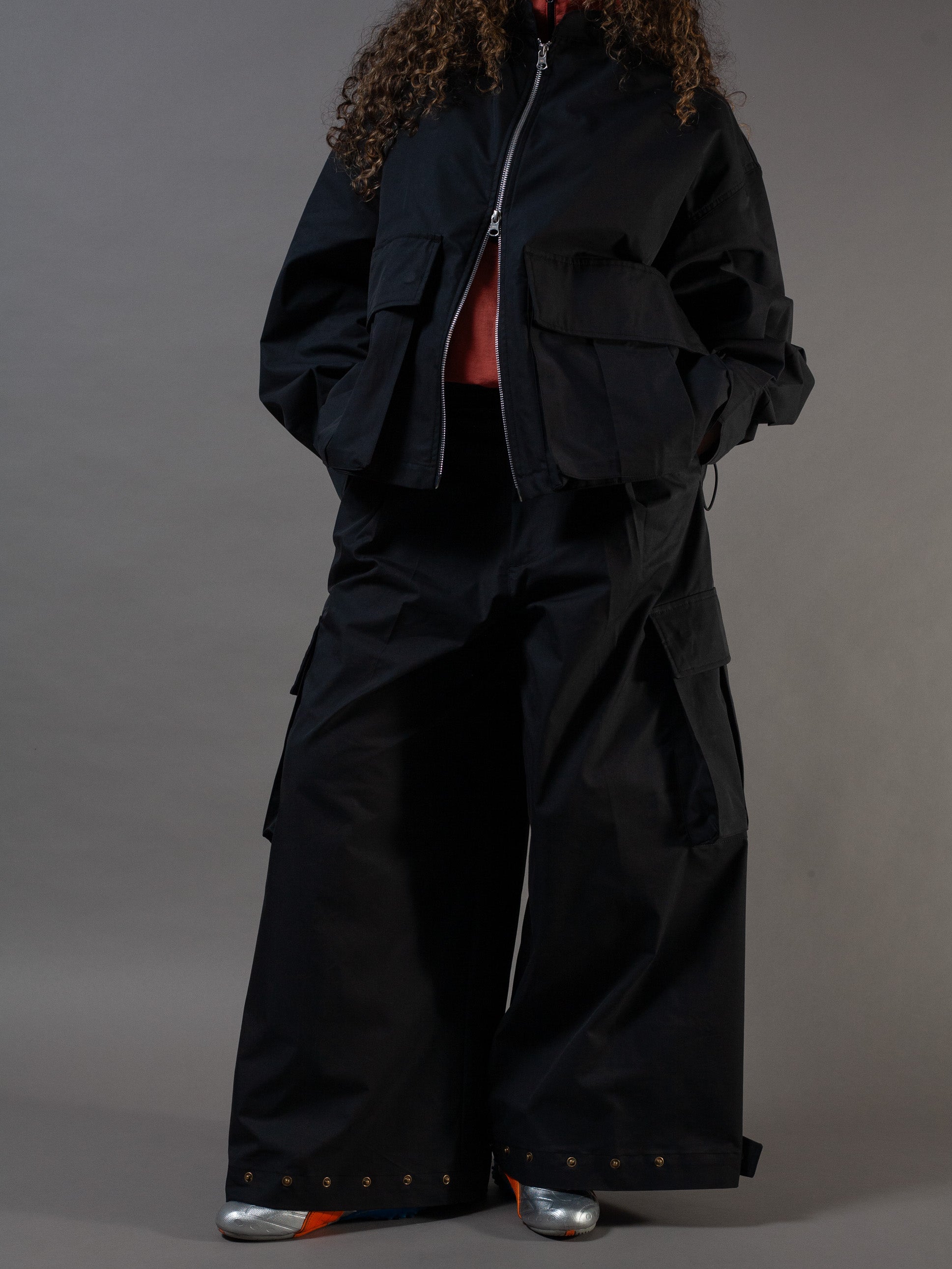 Person wearing a black outfit with wide-leg pants and a jacket on a gray background