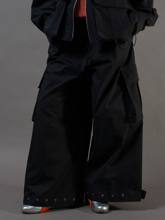 Person wearing a black outfit with wide-leg pants and a jacket on a gray background