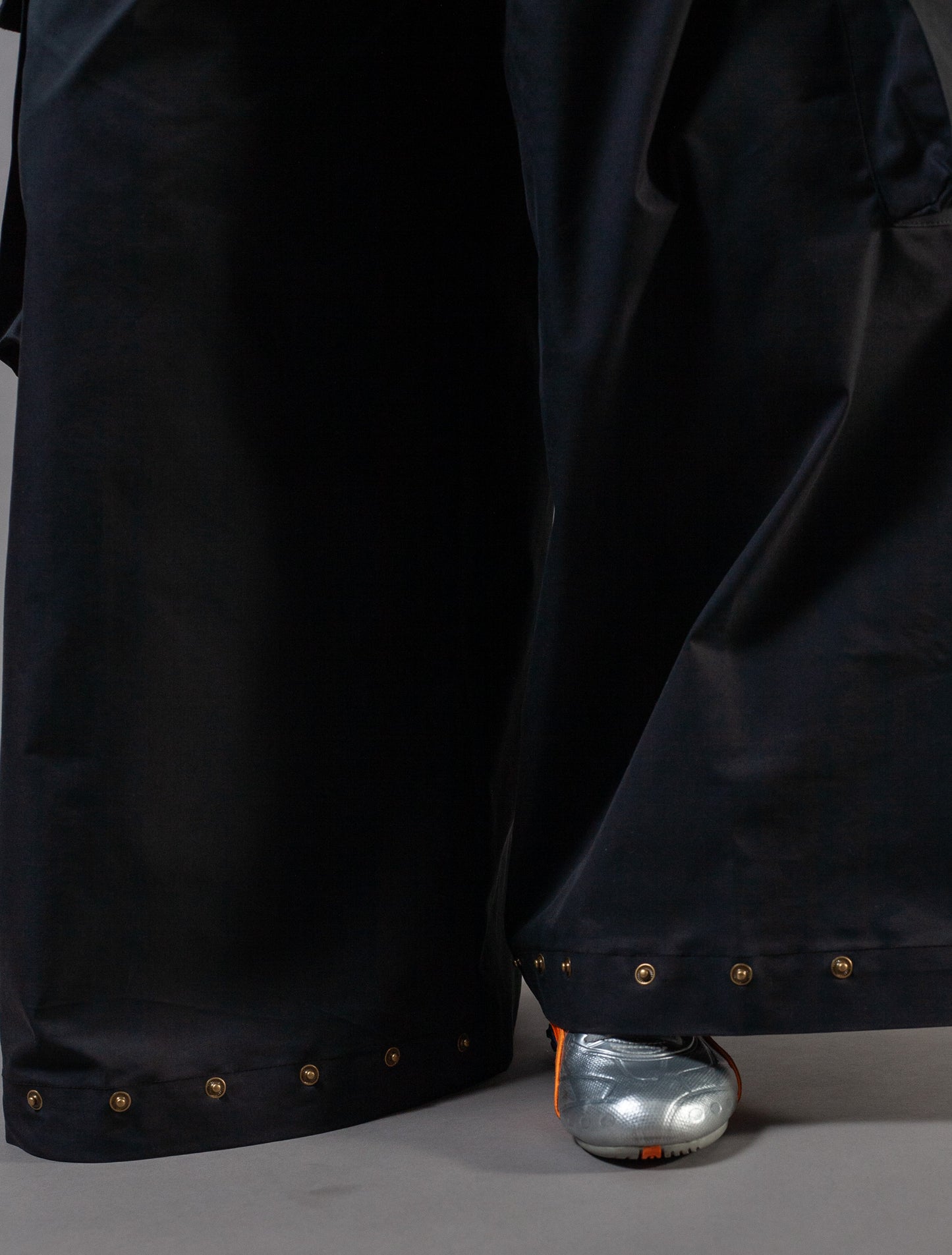 Close-up of black pants with gold press studs on a gray background