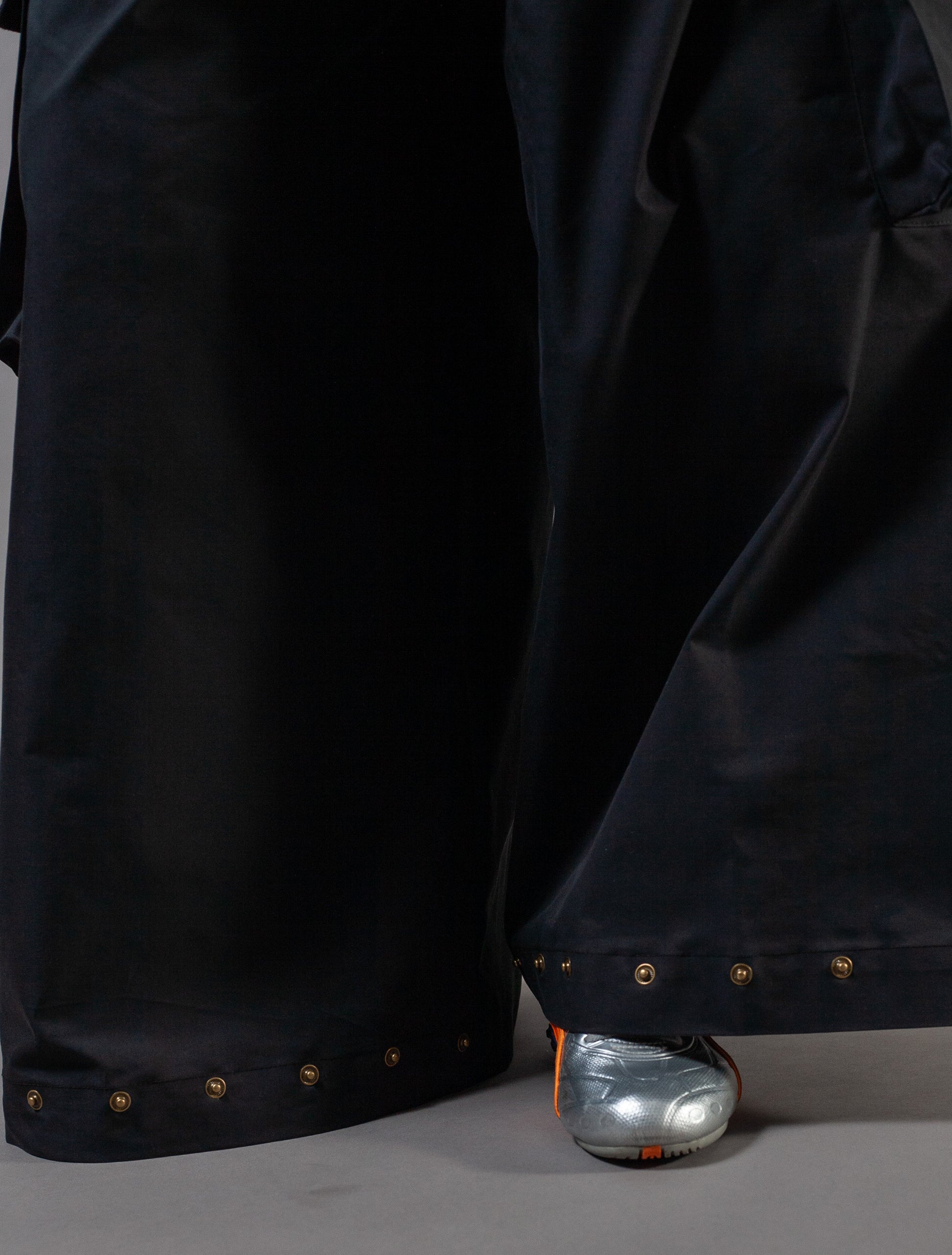 Close-up of black pants with gold press studs on a gray background