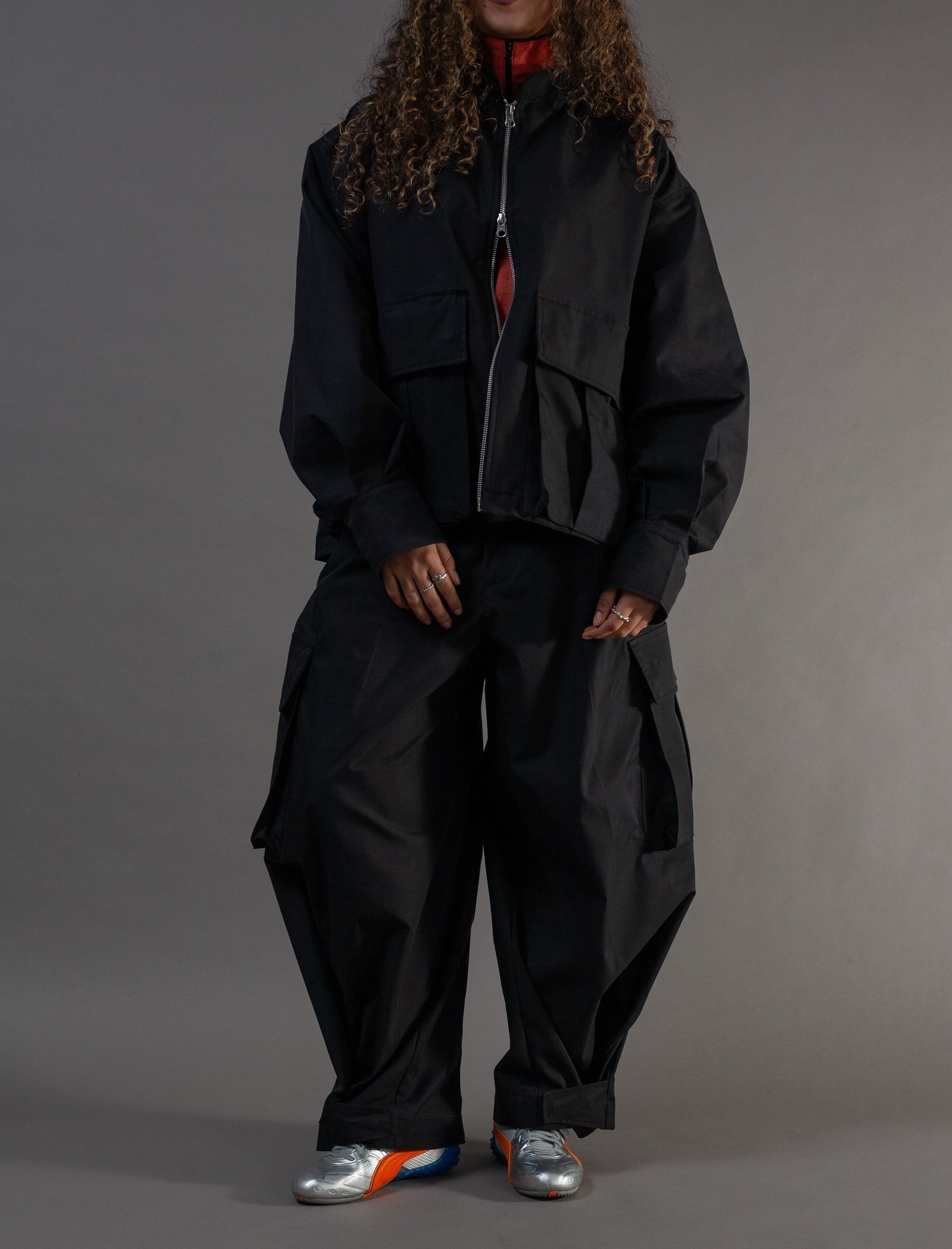 Person wearing a black outfit with a jacket and pants on a gray background
