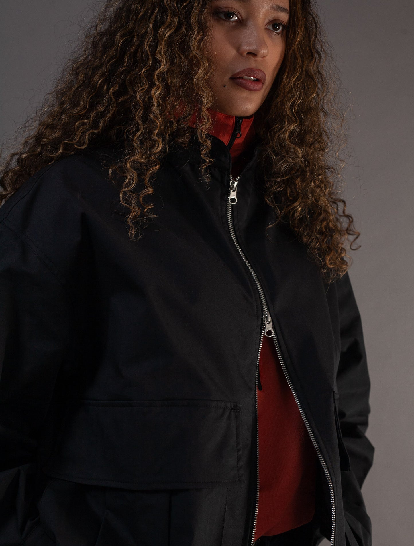 Person wearing a black jacket with a orange top underneath on a gray background