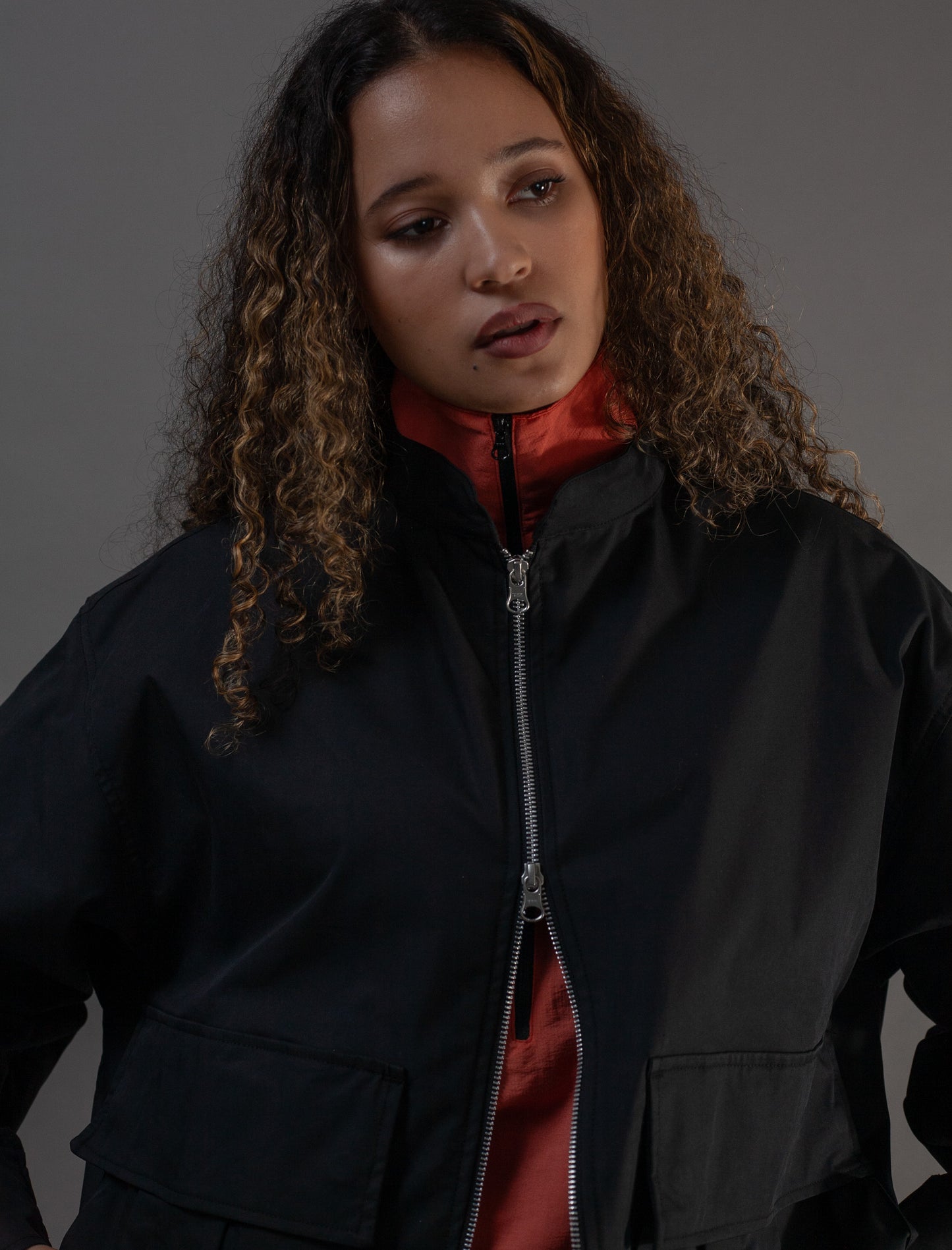 Woman wearing a black jacket over a orange garment against a gray background