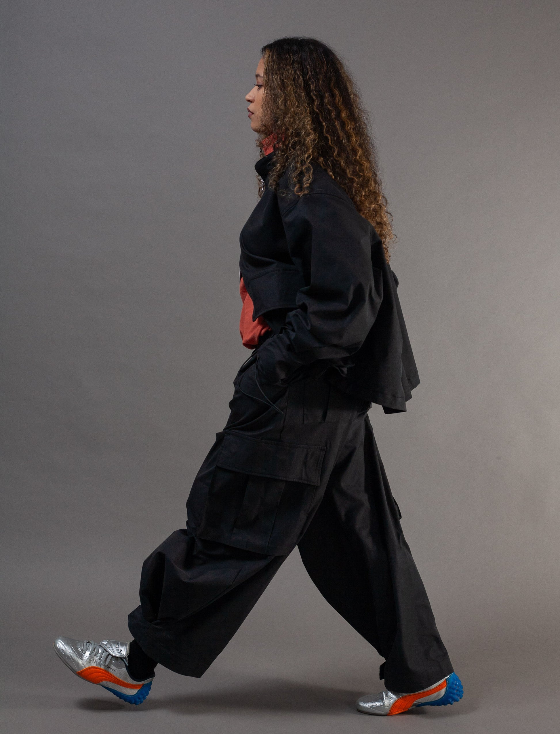 Person wearing a black outfit with colorful shoes on a gray background