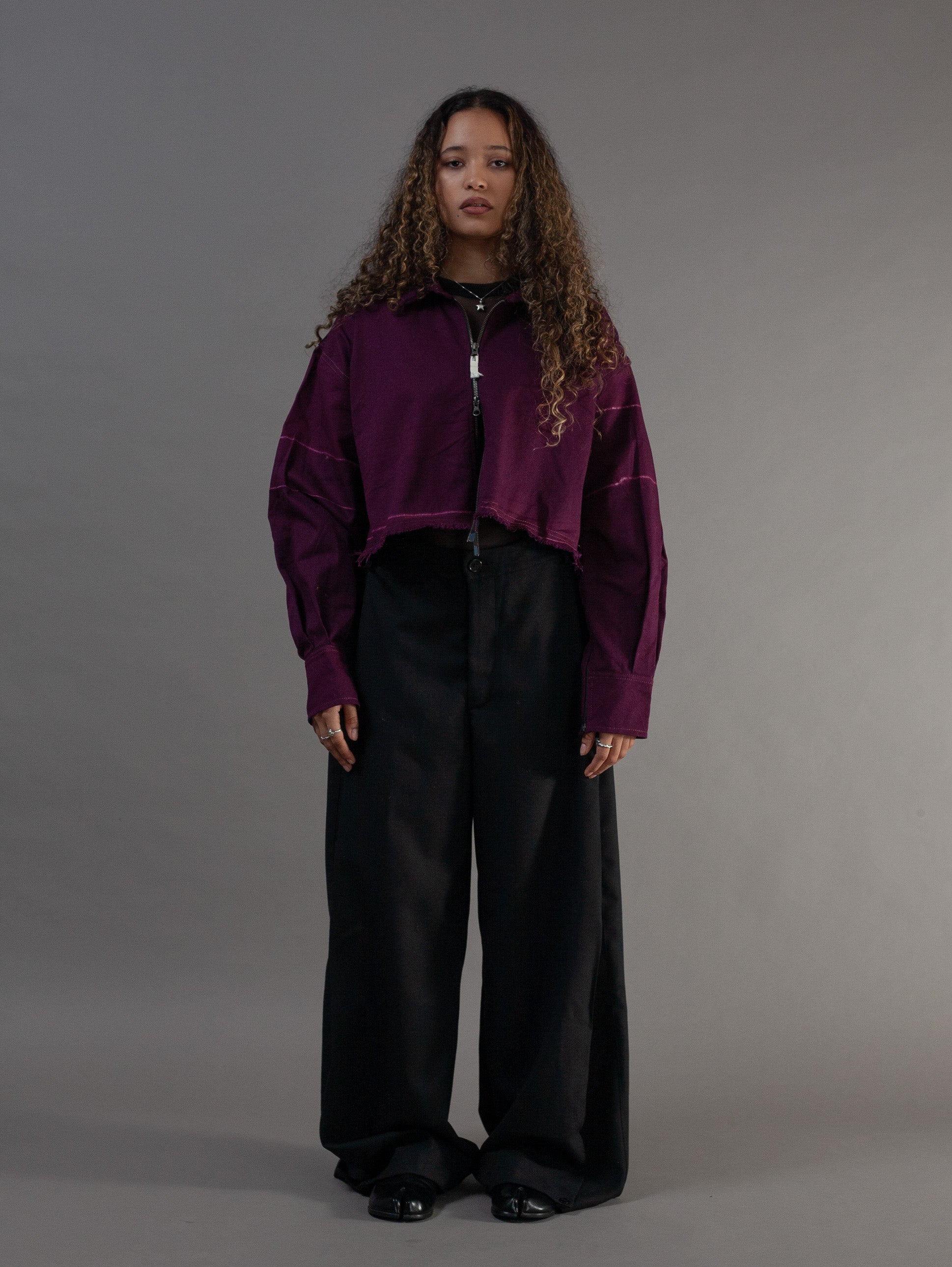 Person wearing a purple jacket and black pants against a gray background