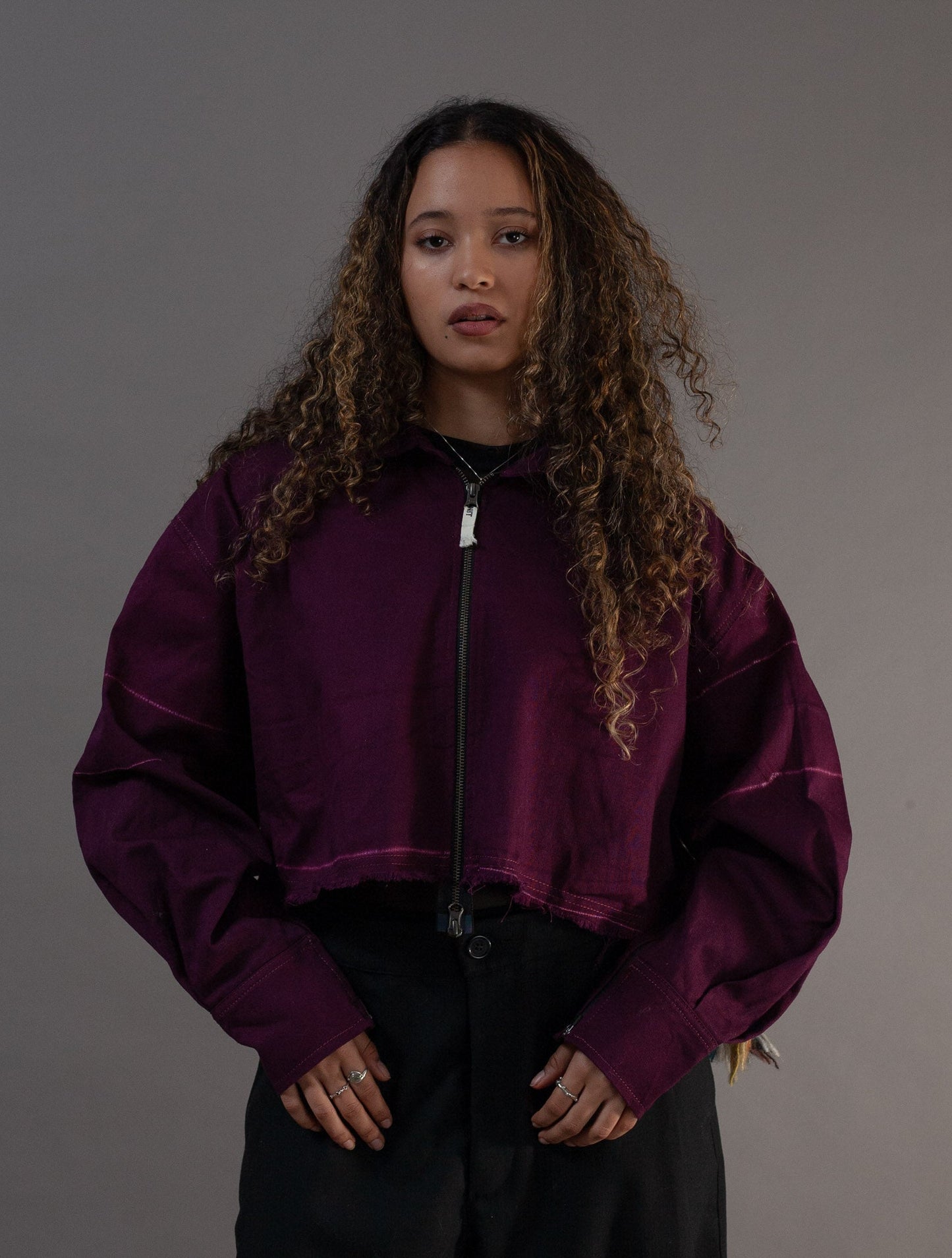 Person wearing a purple jacket and black pants against a gray background