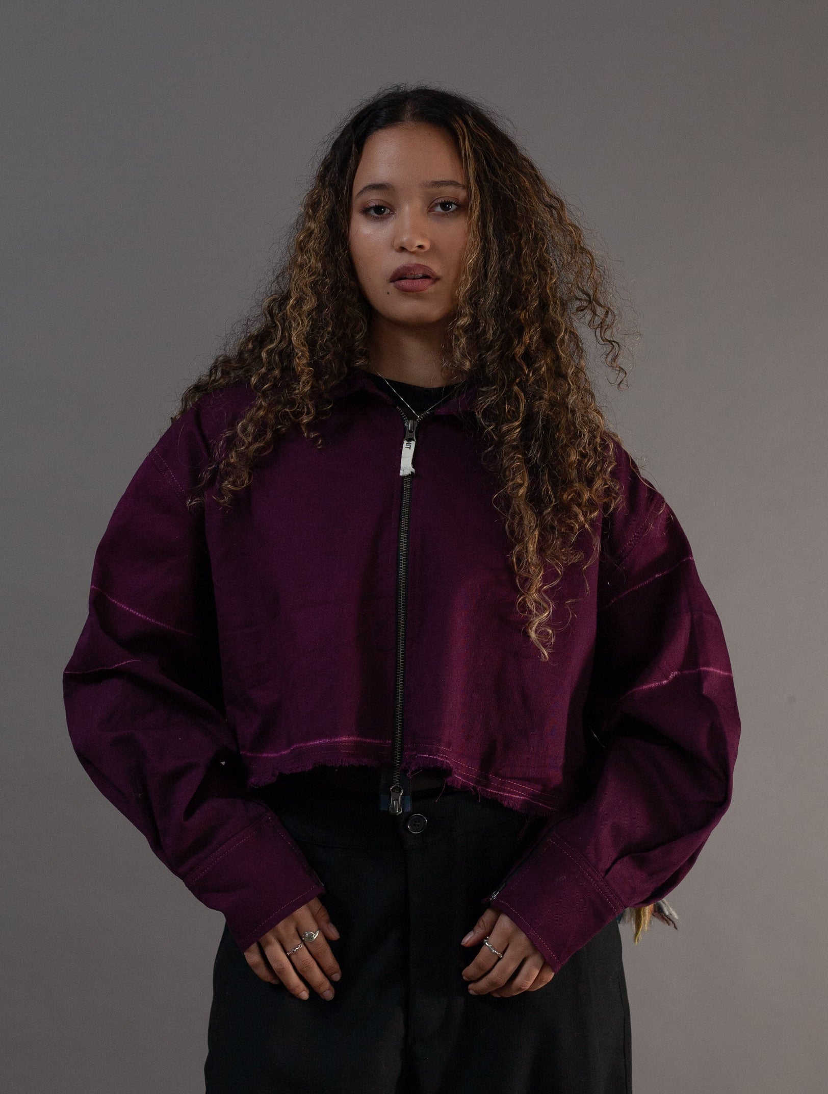 Person wearing a purple jacket and black pants against a gray background