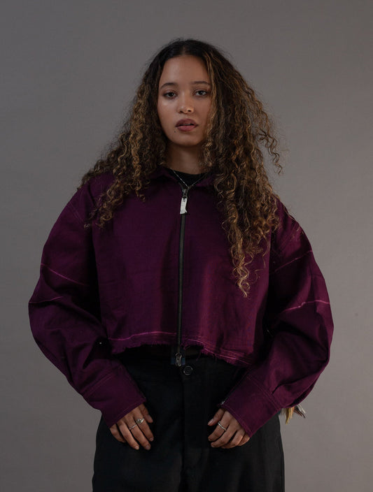 Person wearing a purple jacket and black pants against a gray background