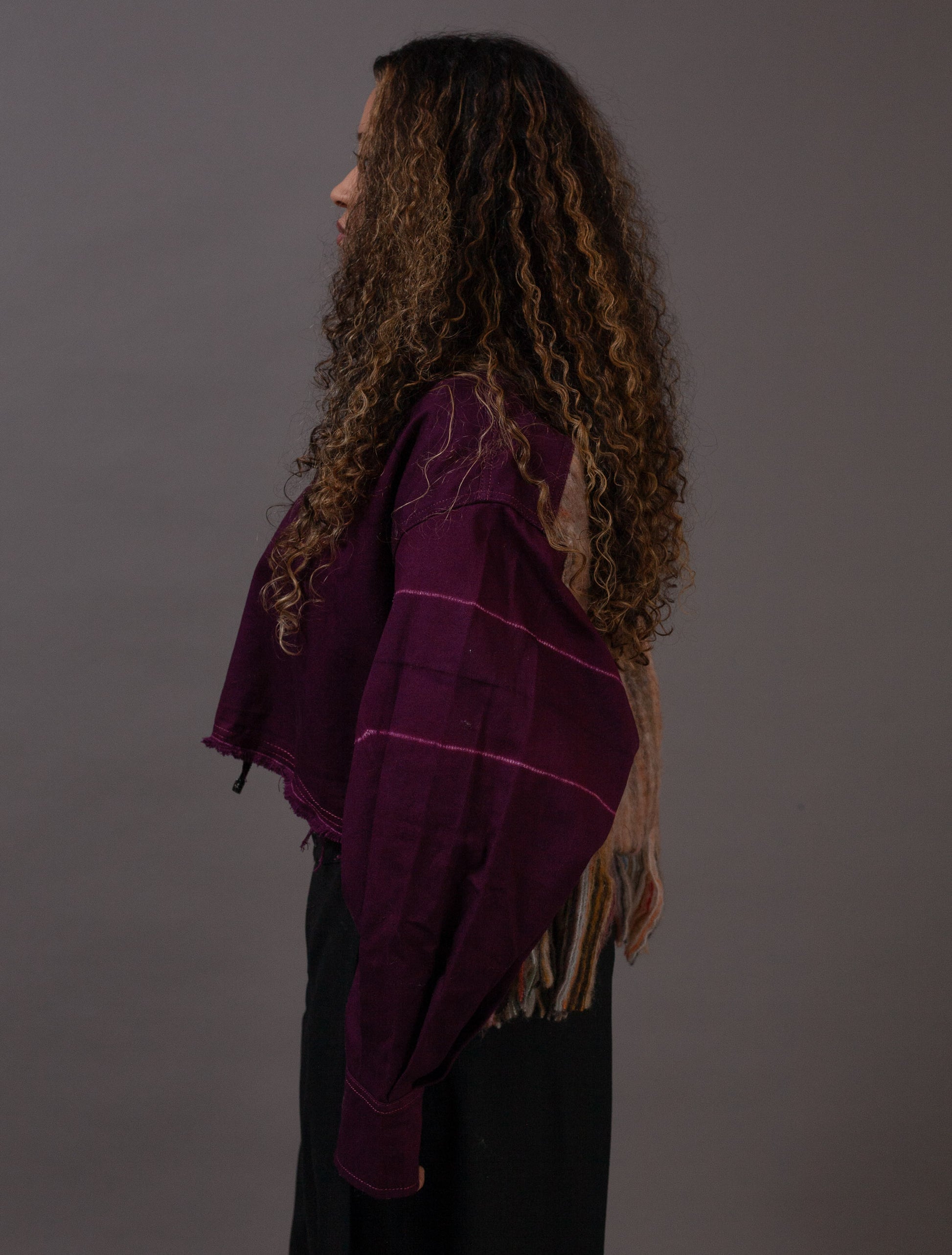 Person wearing a purple shawl with wool fringe on a gray background