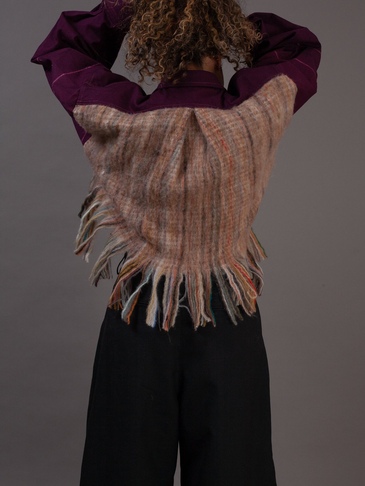 Person wearing a purple jacket with fringe, standing against a plain background