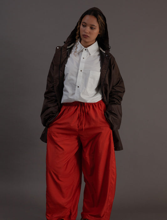 Person wearing a white shirt and orange pants with a brown rain jacket on a gray background