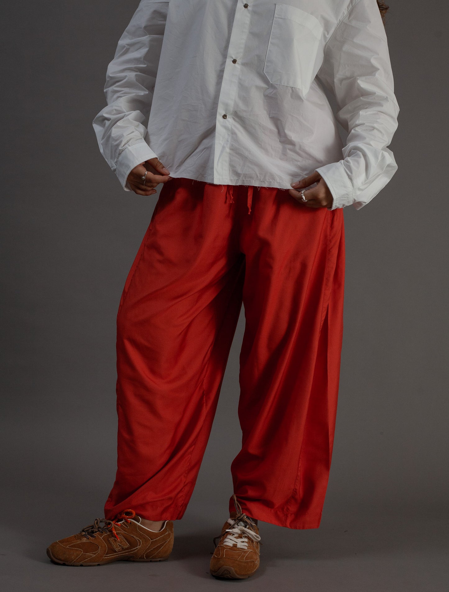Person wearing a white shirt and orange pants on a gray background
