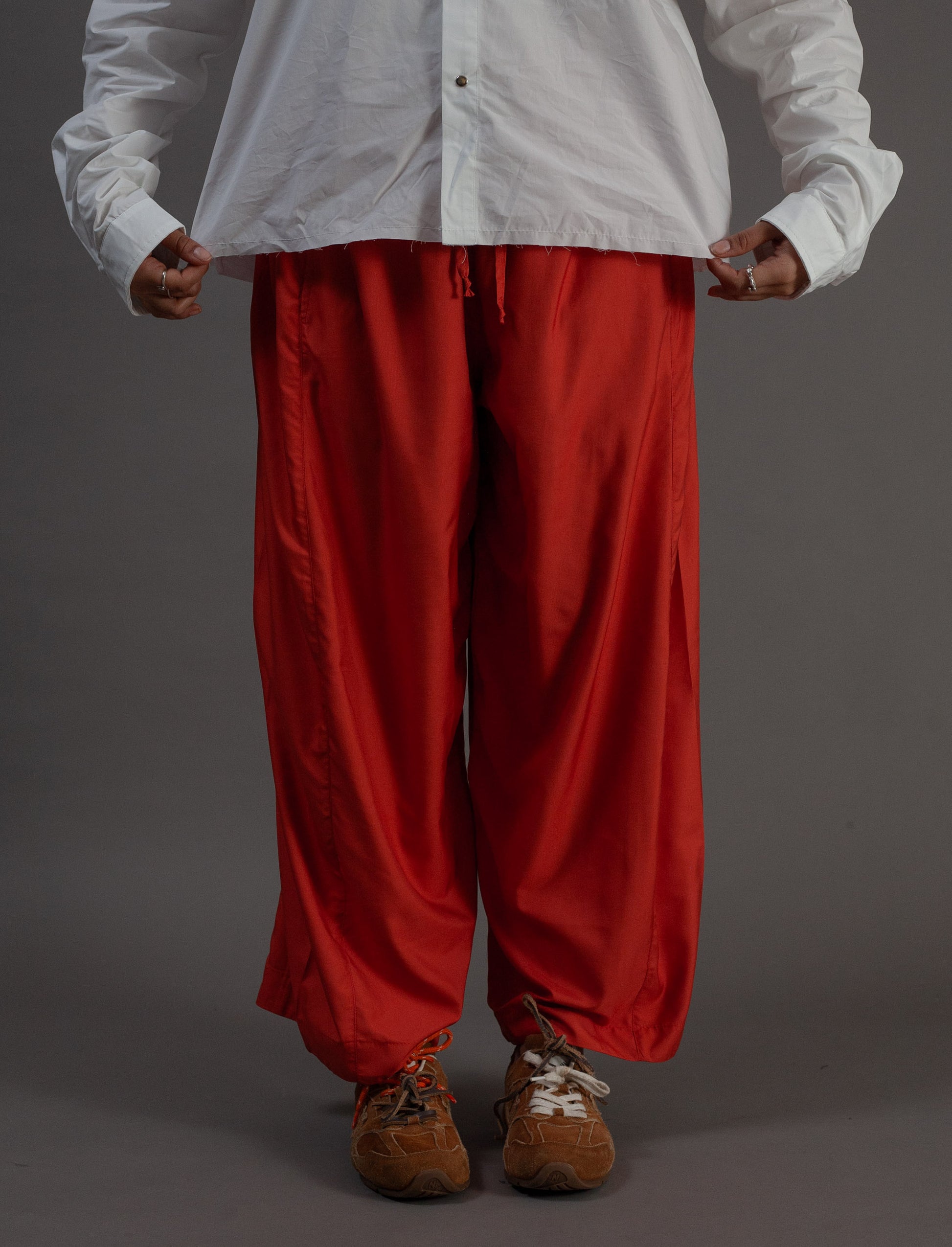 Person wearing a white shirt and orange pants on a gray background
