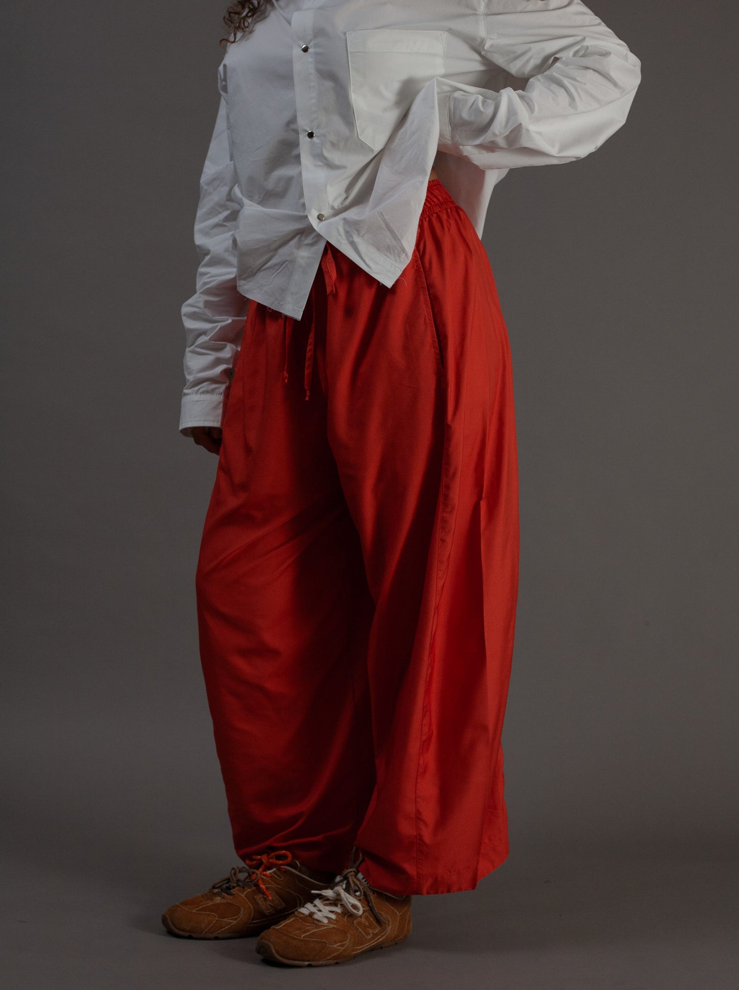 Person wearing a white shirt and orange pants on a gray background
