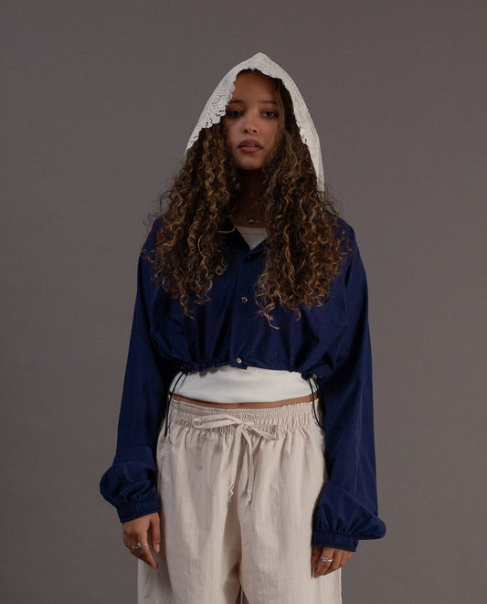 Person wearing a blue jacket with a hood and beige pants on a gray background