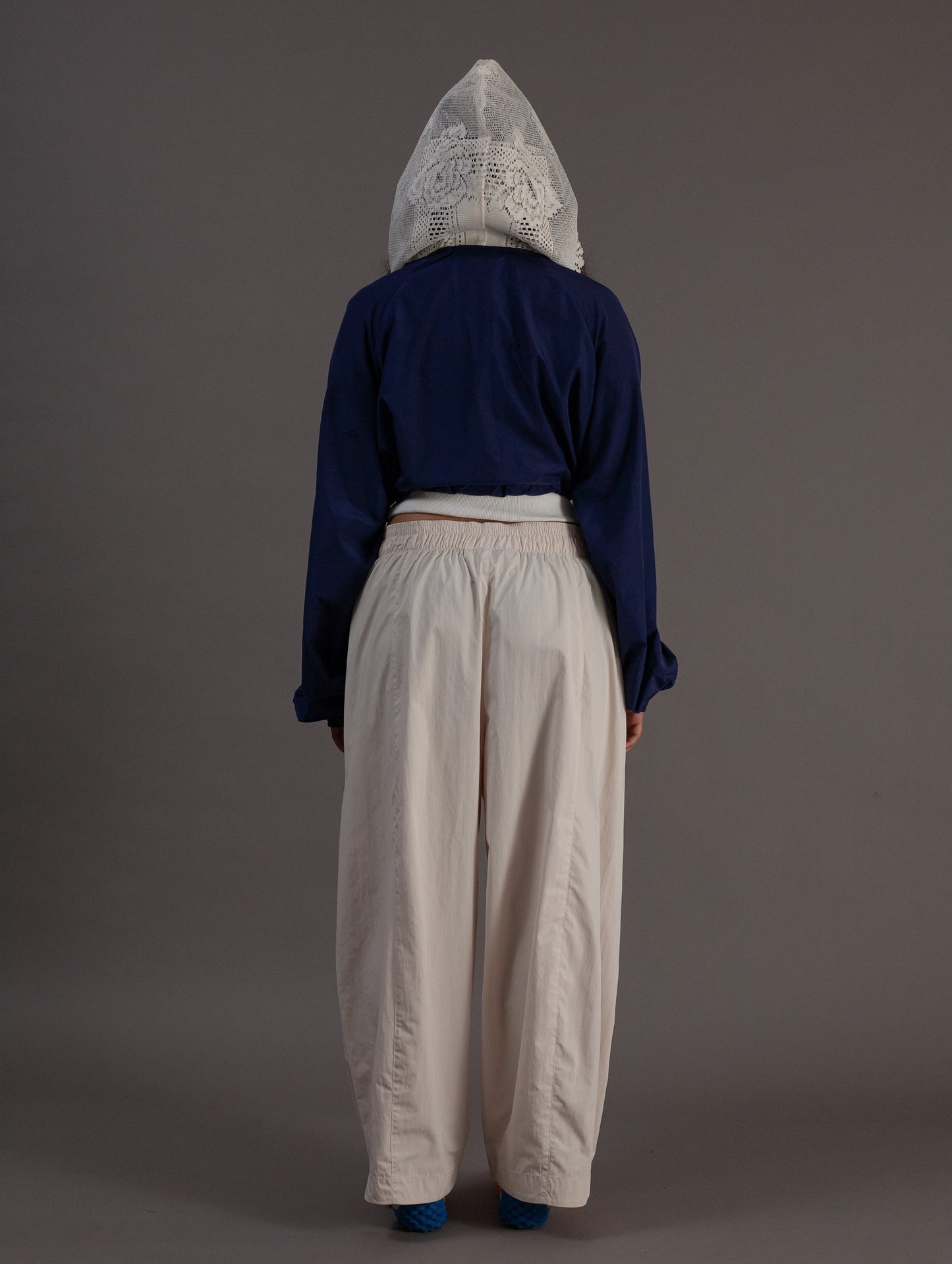 Person wearing a blue top and beige pants with a hood on a gray background