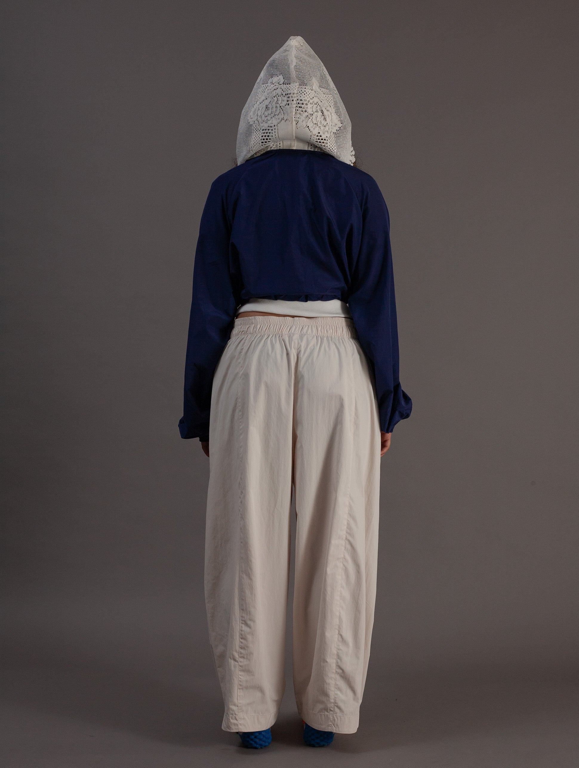 Person wearing a blue top and beige pants with a hood on a gray background
