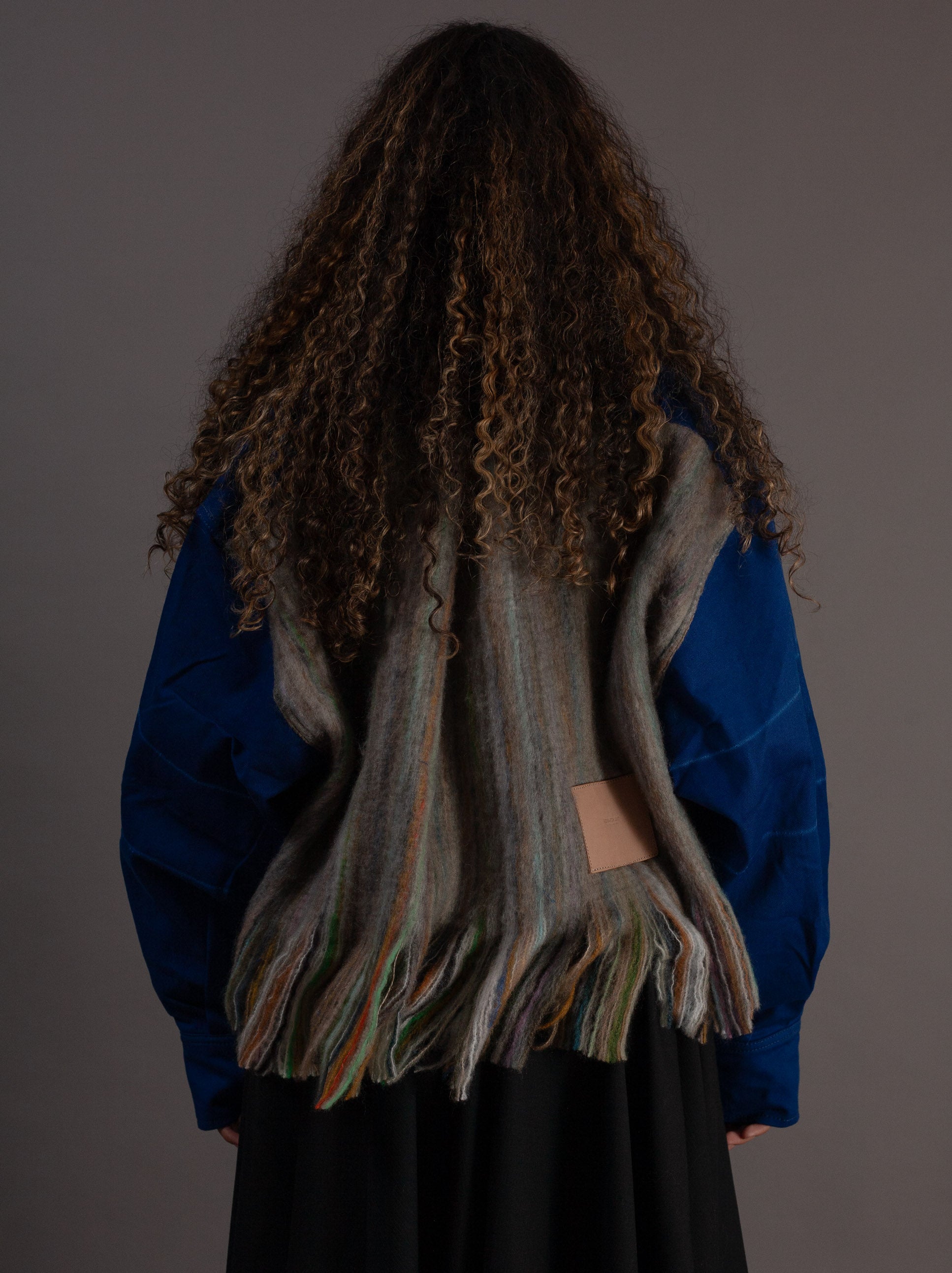 Person wearing a blue jacket and a long, wool back against a plain background