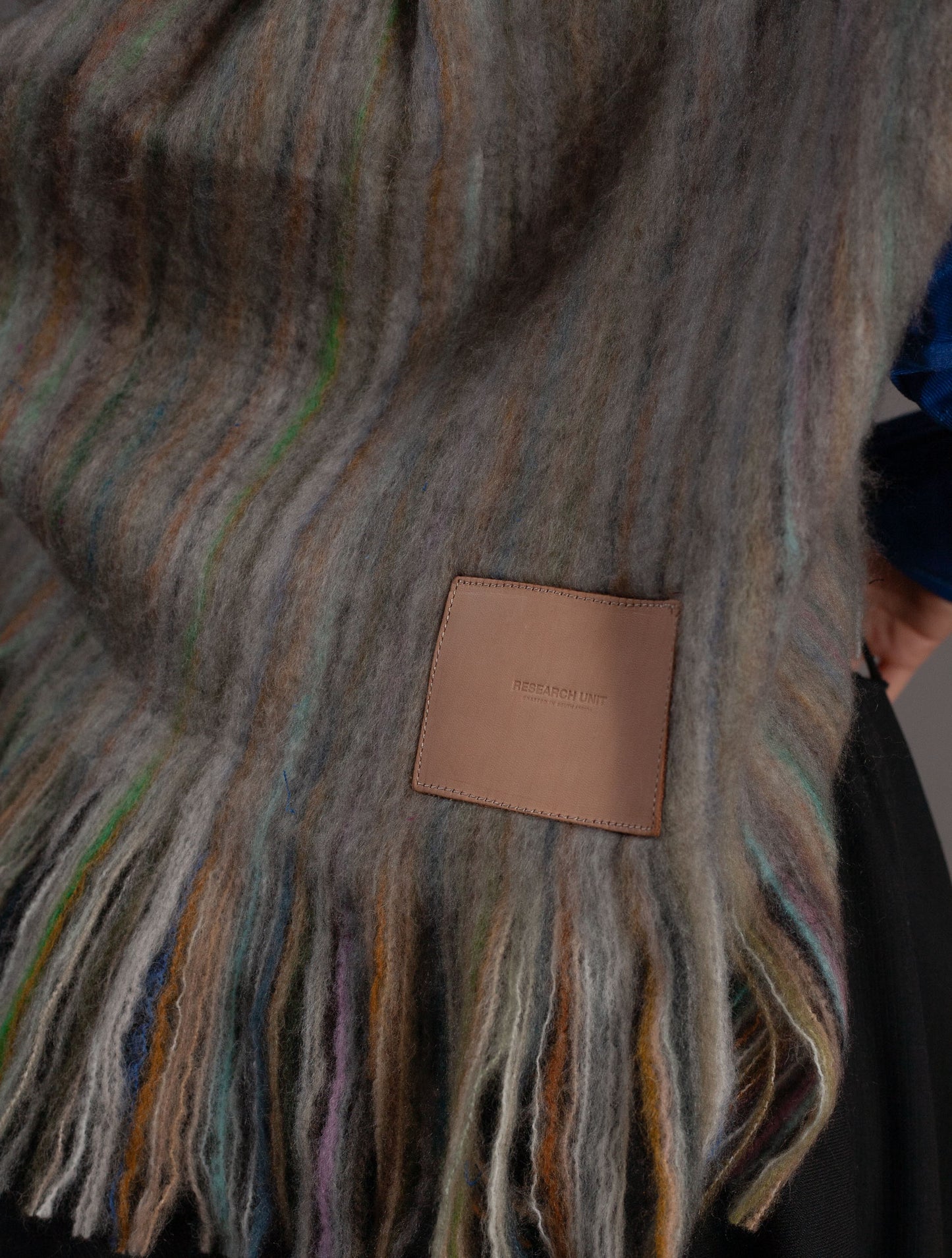 Multicolored striped wool blanket with a brand label held by a person wearing a blue shirt.