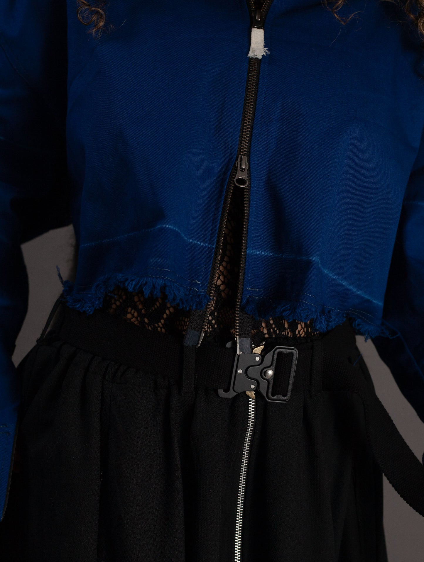 Close-up of a blue jacket with a black zipper and lace top on a gray background
