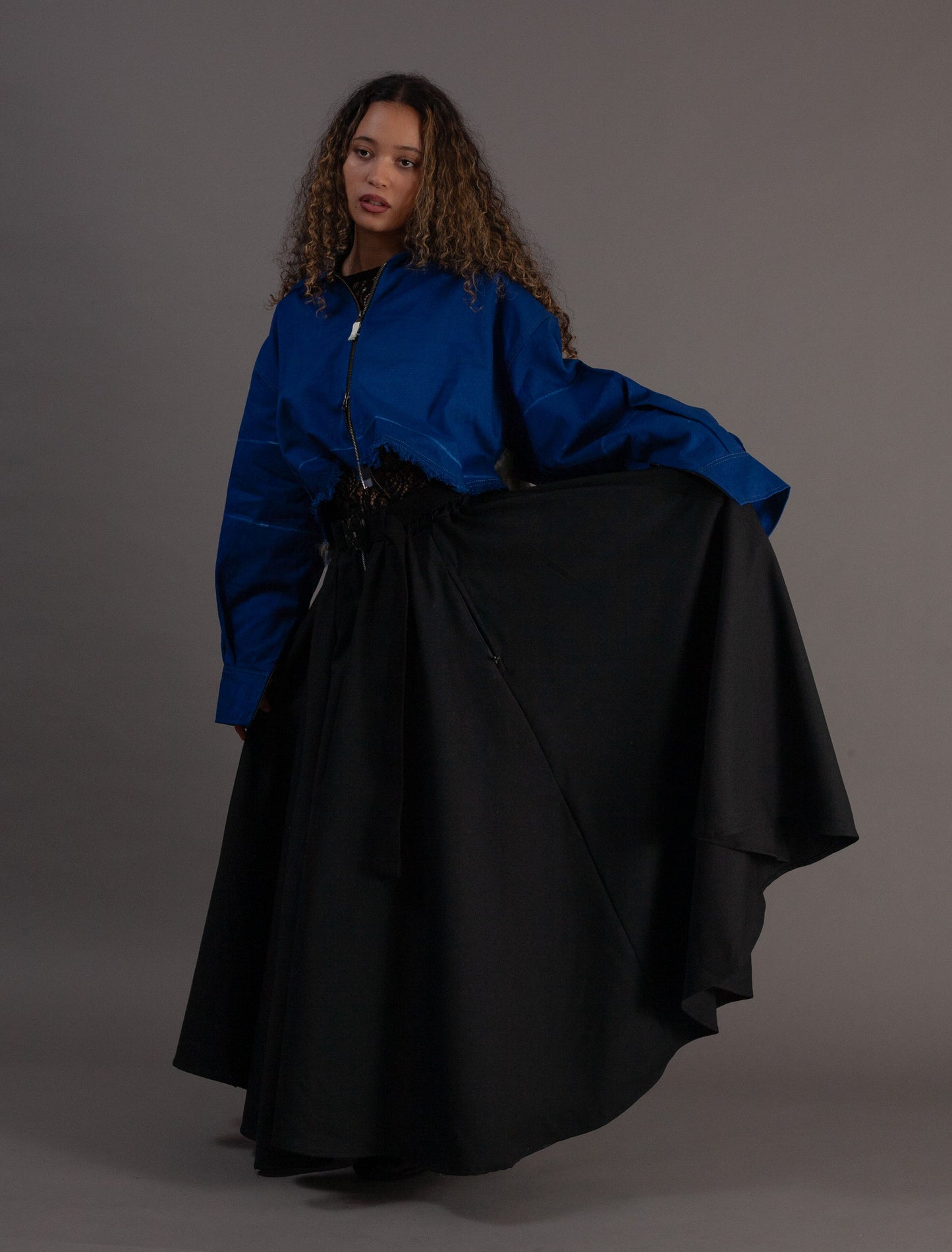 Person wearing a blue jacket and black skirt against a gray background