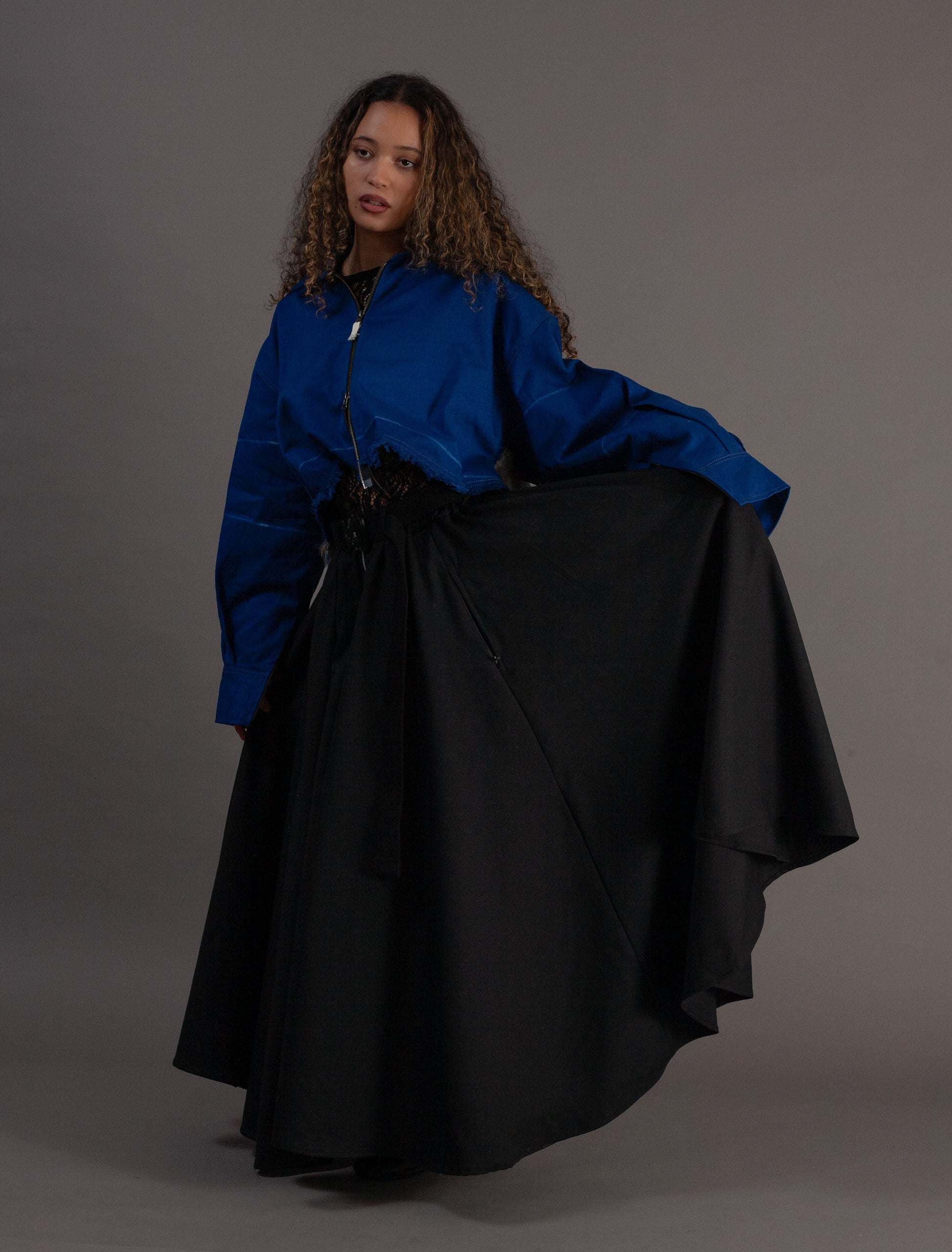 Person wearing a blue jacket and black skirt against a gray background