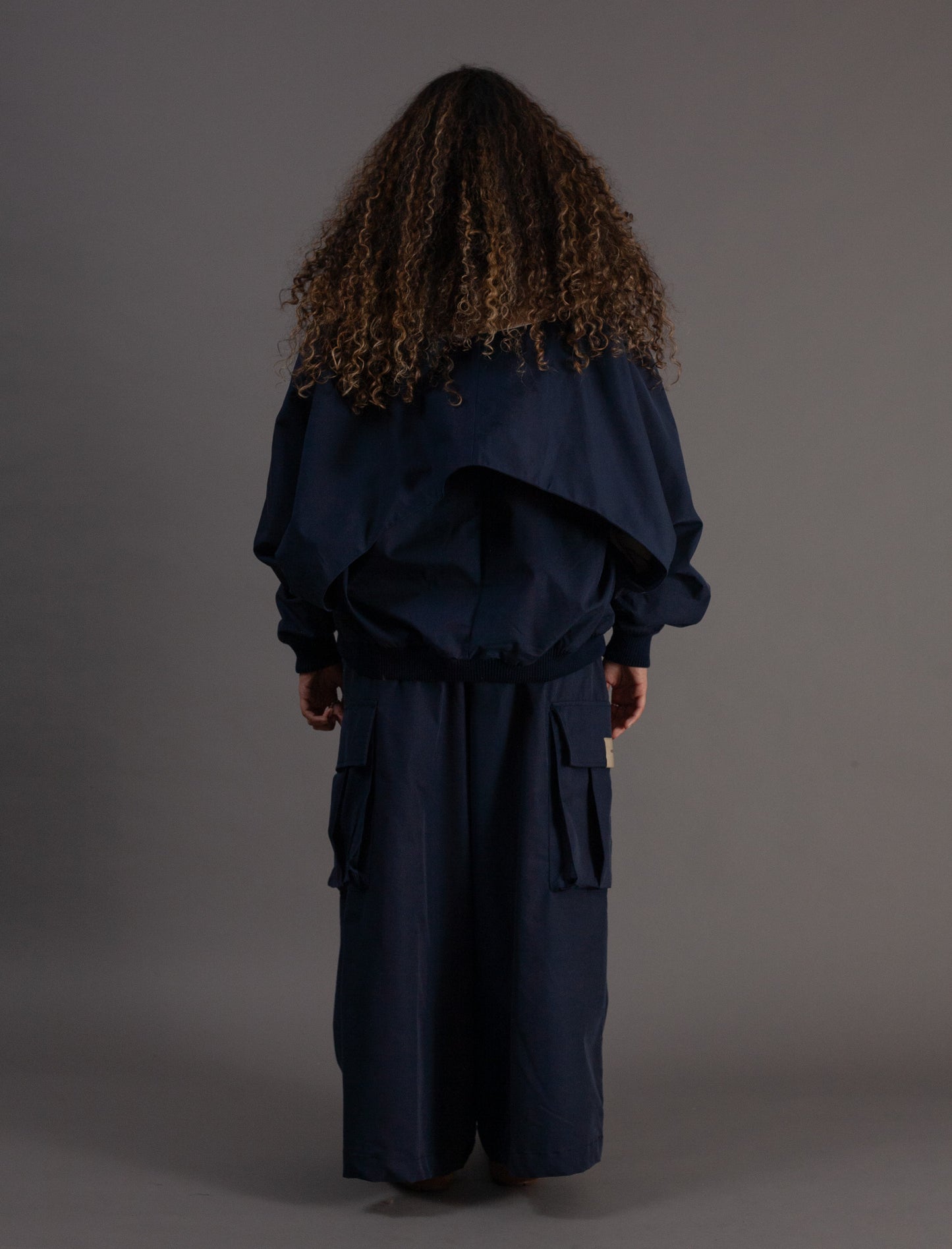 Person wearing a navy blue outfit with a hood on a gray background