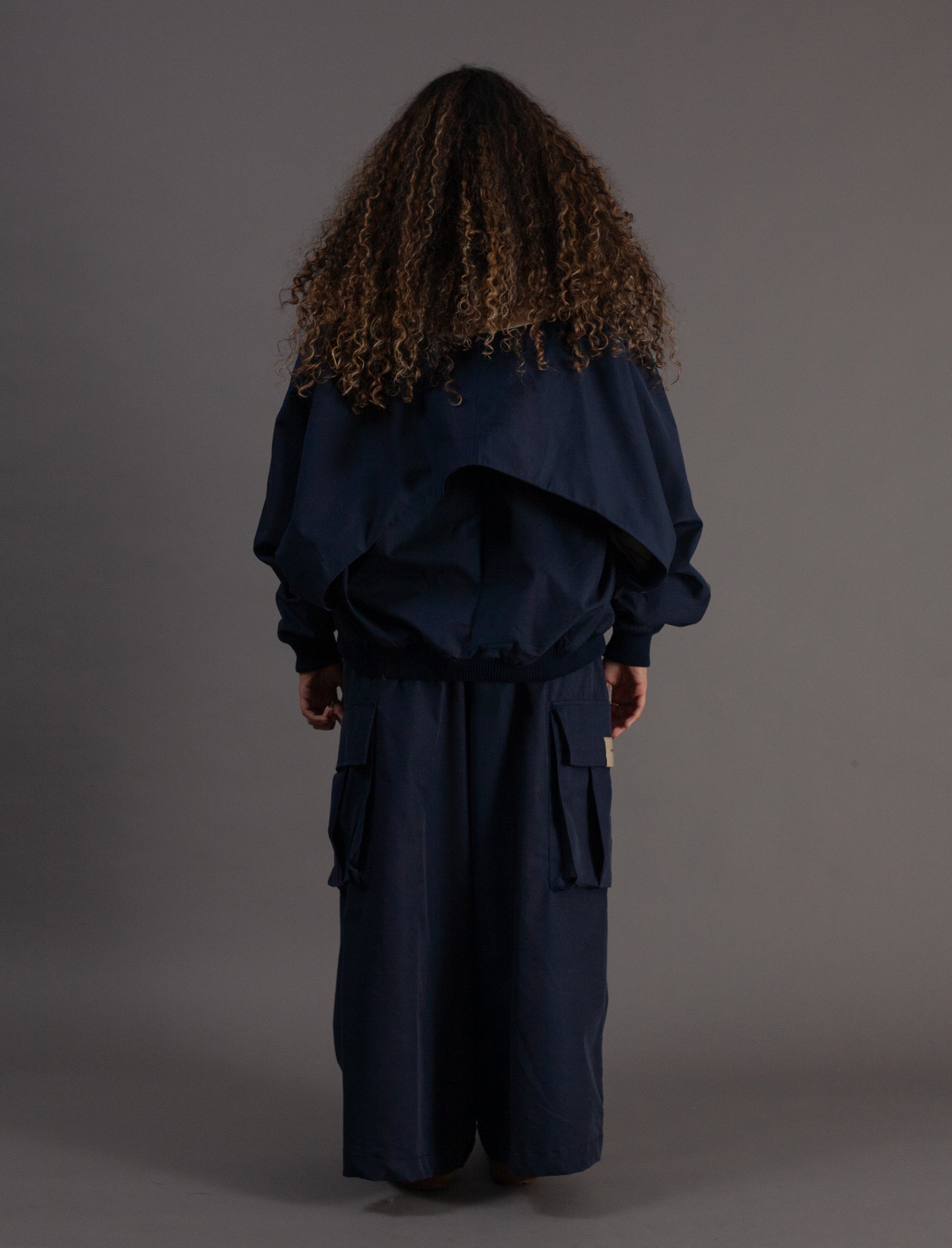 Person wearing a navy blue outfit with a hood on a gray background