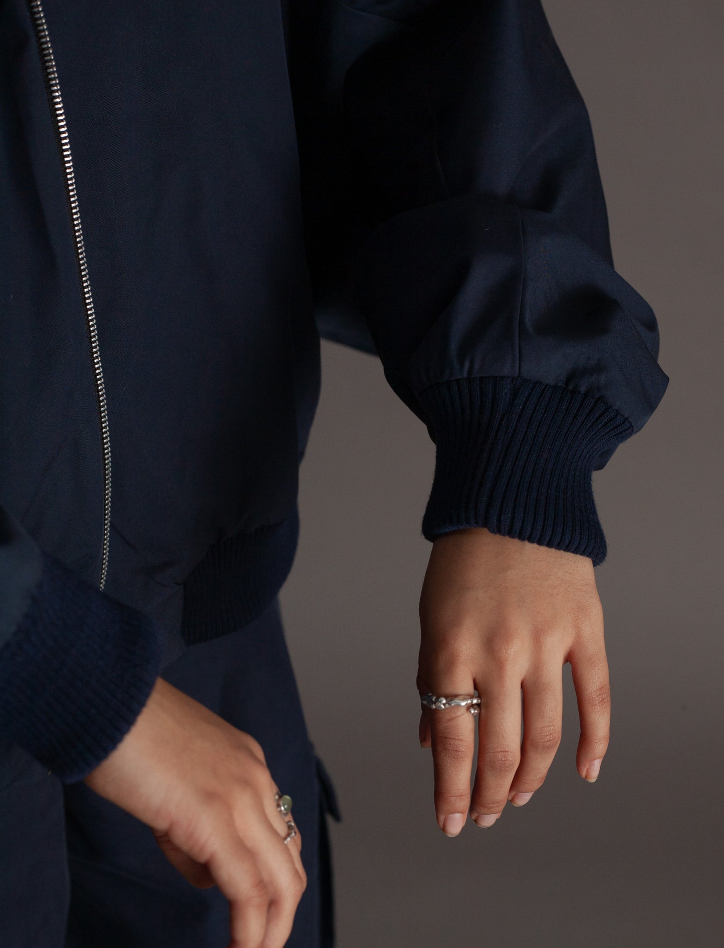Navy blue jacket with a person wearing it, showing a close-up of the sleeve and hand.